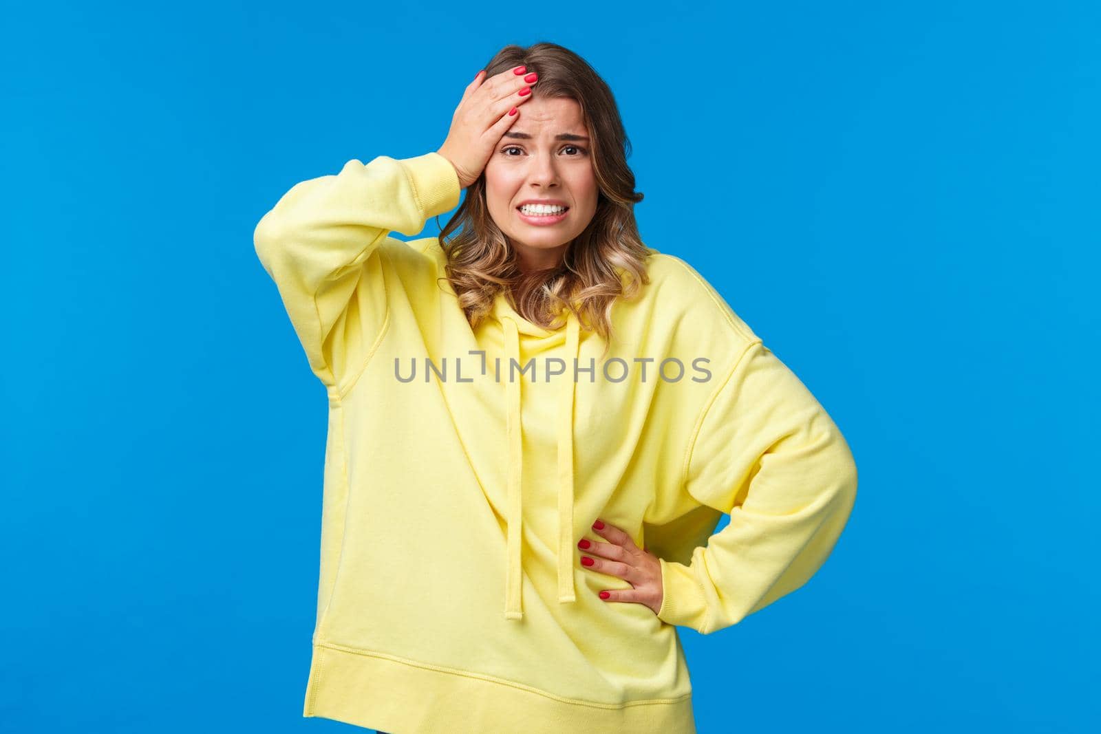 Embarrassed and worried girl bumped into car, feel anxious and concerned, touch head troubled, grimacing with awkward grin, face problematic situation, stand blue background by Benzoix
