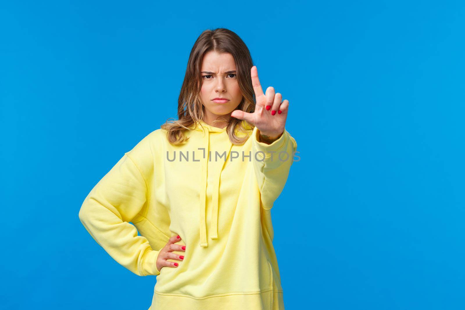 Stop right there. Serious-looking angry and bossy elder sister prohibit something, scolding kid as shaking finger with disapproval or disagreement, standing blue background by Benzoix