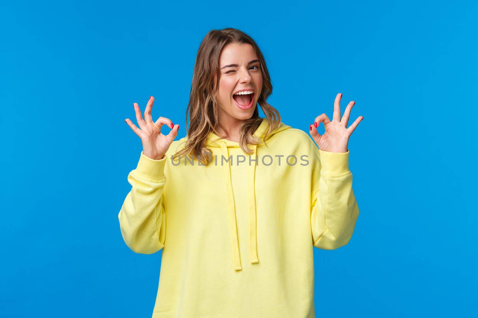 Girl assure she will deal with problem, nothing worry about. Blond female student guarantee everything good, wink and smiling relaxed, show okay gesture, standing blue background.