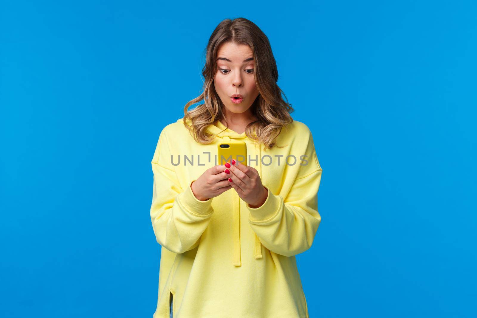 Surprised and intrigued good-looking blond female seeing something interesting online, browsing internet searching outfit in clothes store, using cool new application, hold smartphone.