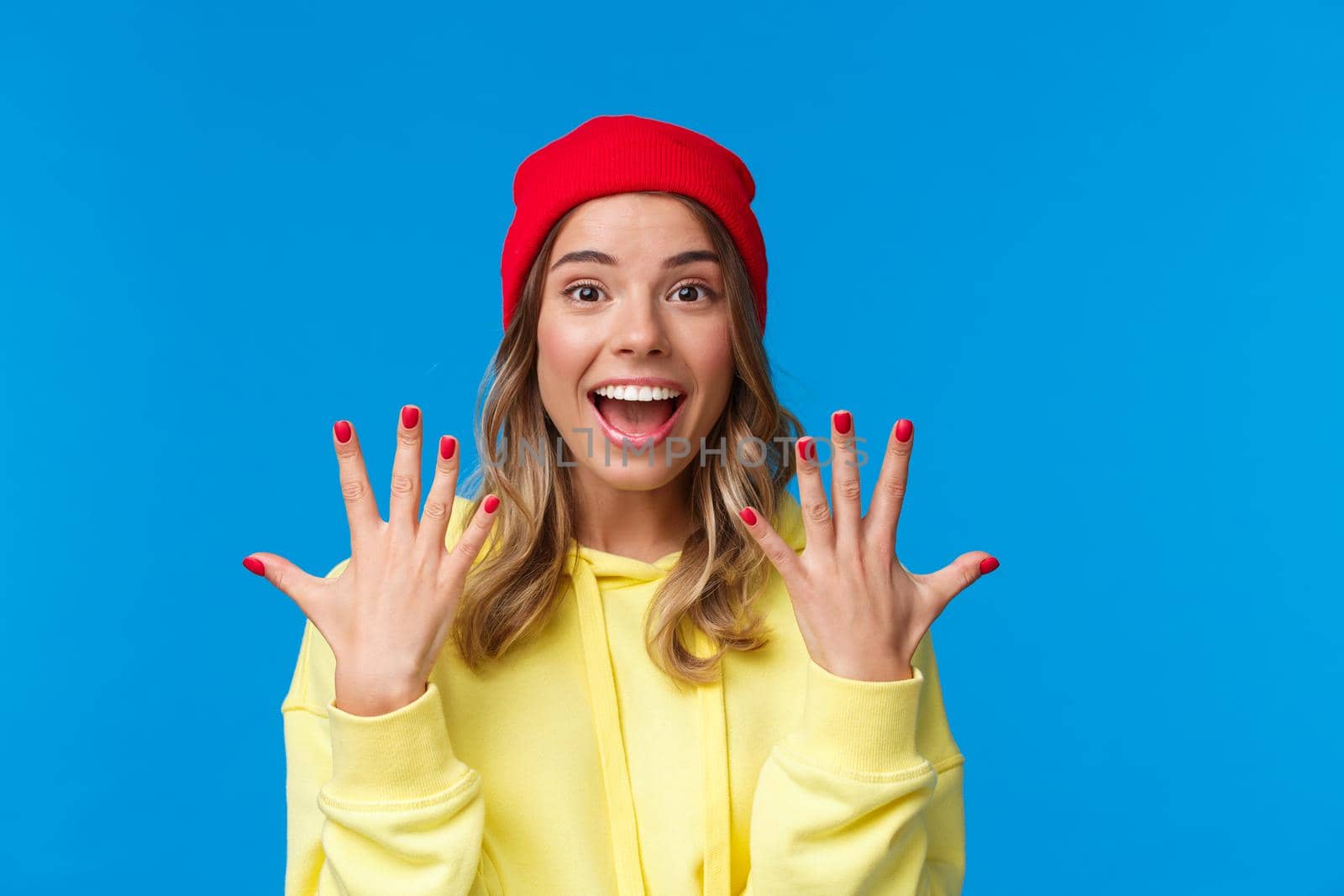 Portrait of amused good-looking blonde hipster girl smiling joyfully, explain something showing number ten, tenth with hands and look camera upbeat, order dozen, stand blue background by Benzoix