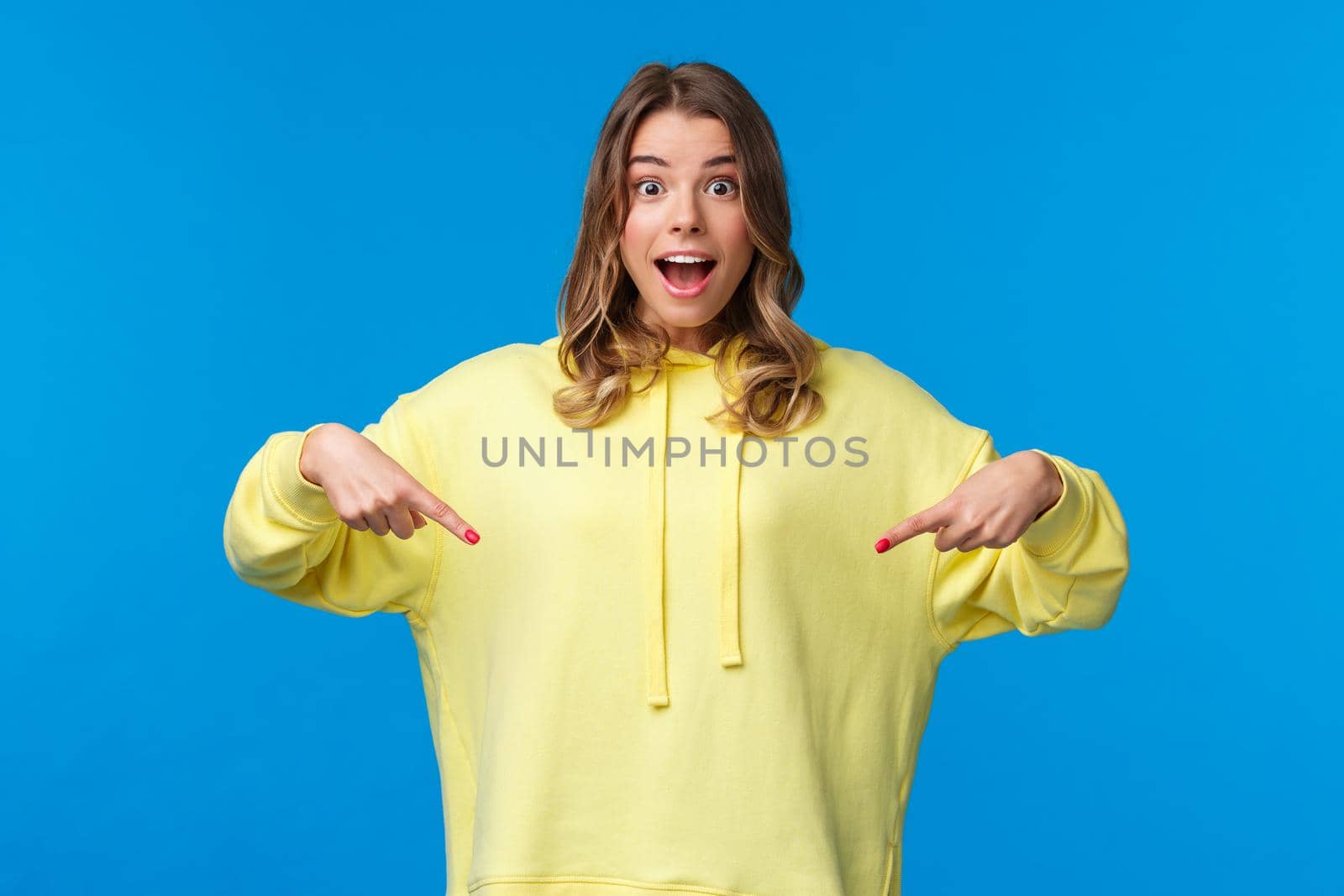 Wow thats something new. Impressed good-looking blond girl telling about awesome promo offer, best discounts, pointing fingers down and looking camera as suggest buy it, blue background.