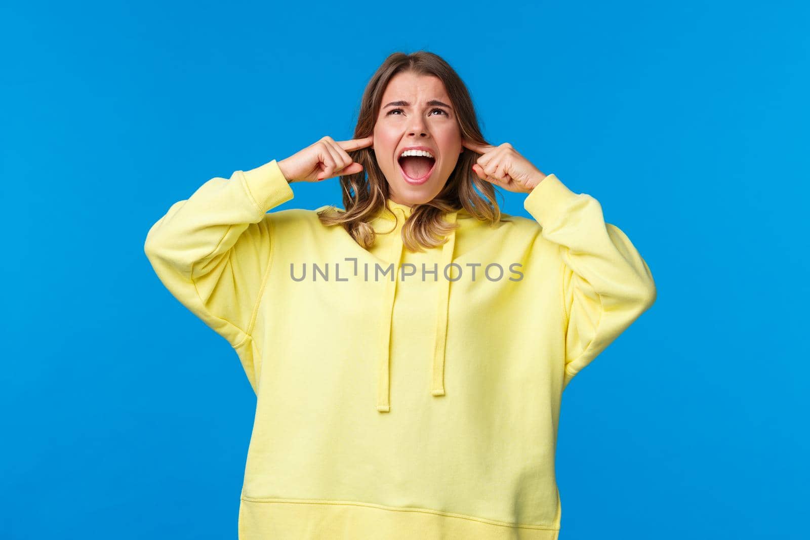 Turn off this awful music. Annoyed and bothered displeased angry blond girl, screaming at ceiling and look up as telling neighbours stop being too loud, shut ears from loud noise.