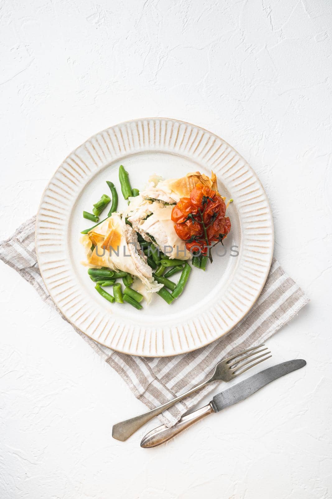 Russian cuisine stuffed chicken cutlets kiev style set, with baked cherry tomatoes And green beans, on white stone background, top view flat lay, with copy space for text