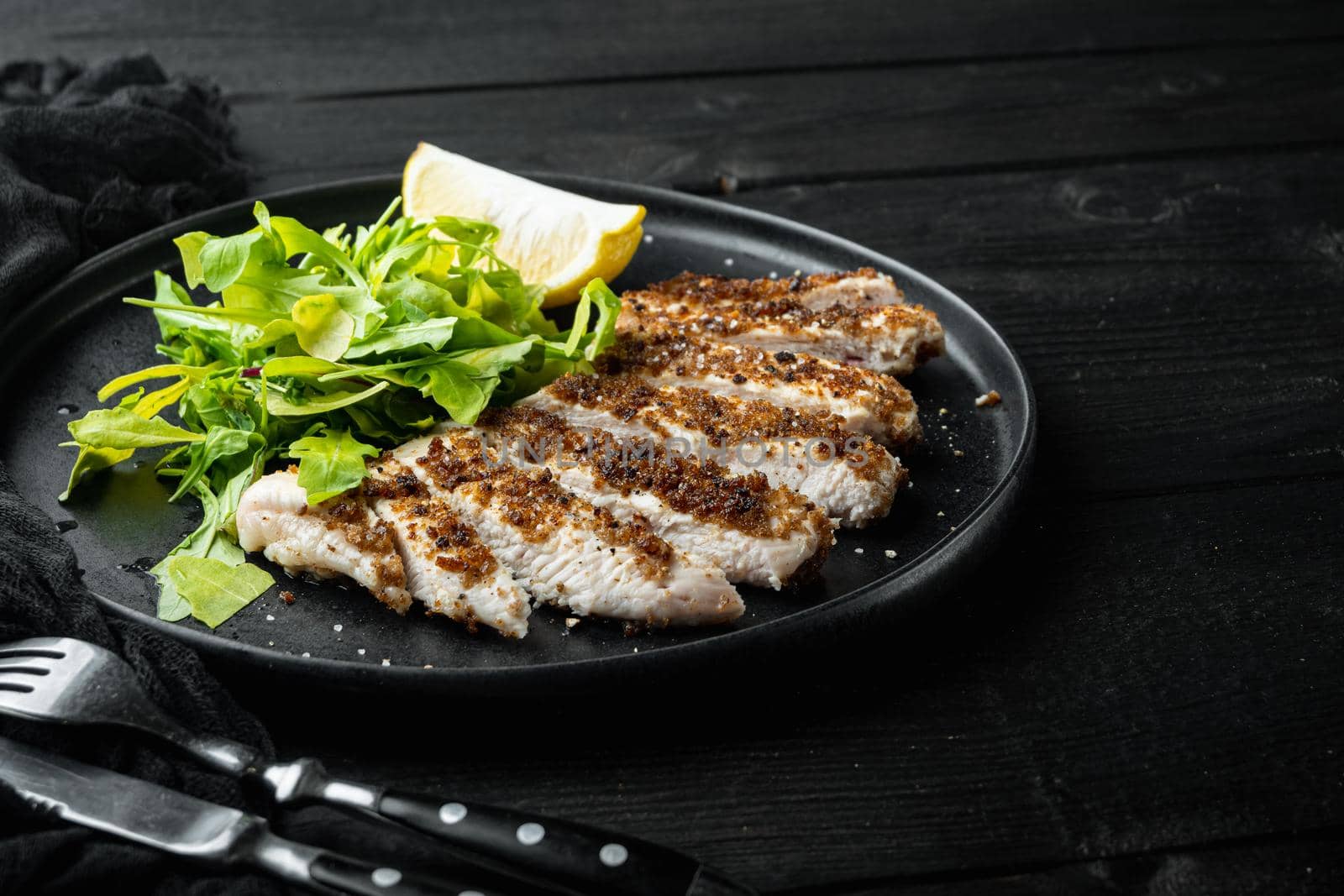 Crumbed, chicken breast fillet grilled, over black wooden table with space for text