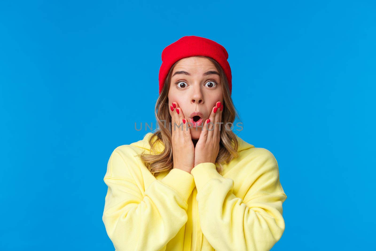 Wow incredible. Impressed and curious good-looking young girl reacting shocked and astonished to interesting awesome news, touch cheeks folding lips stunned, blue background by Benzoix