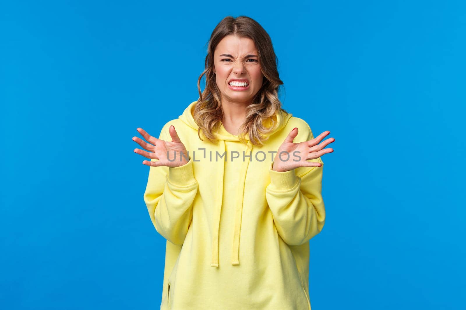 Young woman describing disgusting story, grimacing from aversion and dislike, raising hands and squinting bothered, feel disgust from awful smell or cringy thing she see, blue background by Benzoix