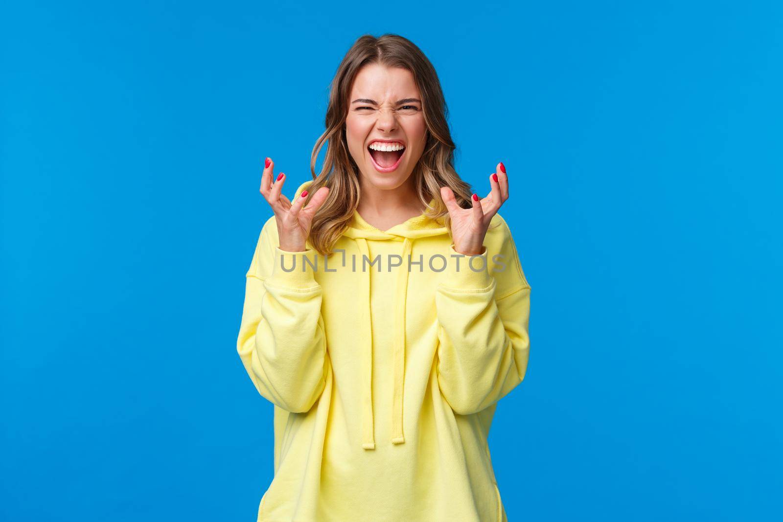 Funny and emotive cute blond european girl in yellow hoodie want squeeze something, clench hands and screaming with grimace, smiling or do evil laugh to scare child with horror story by Benzoix