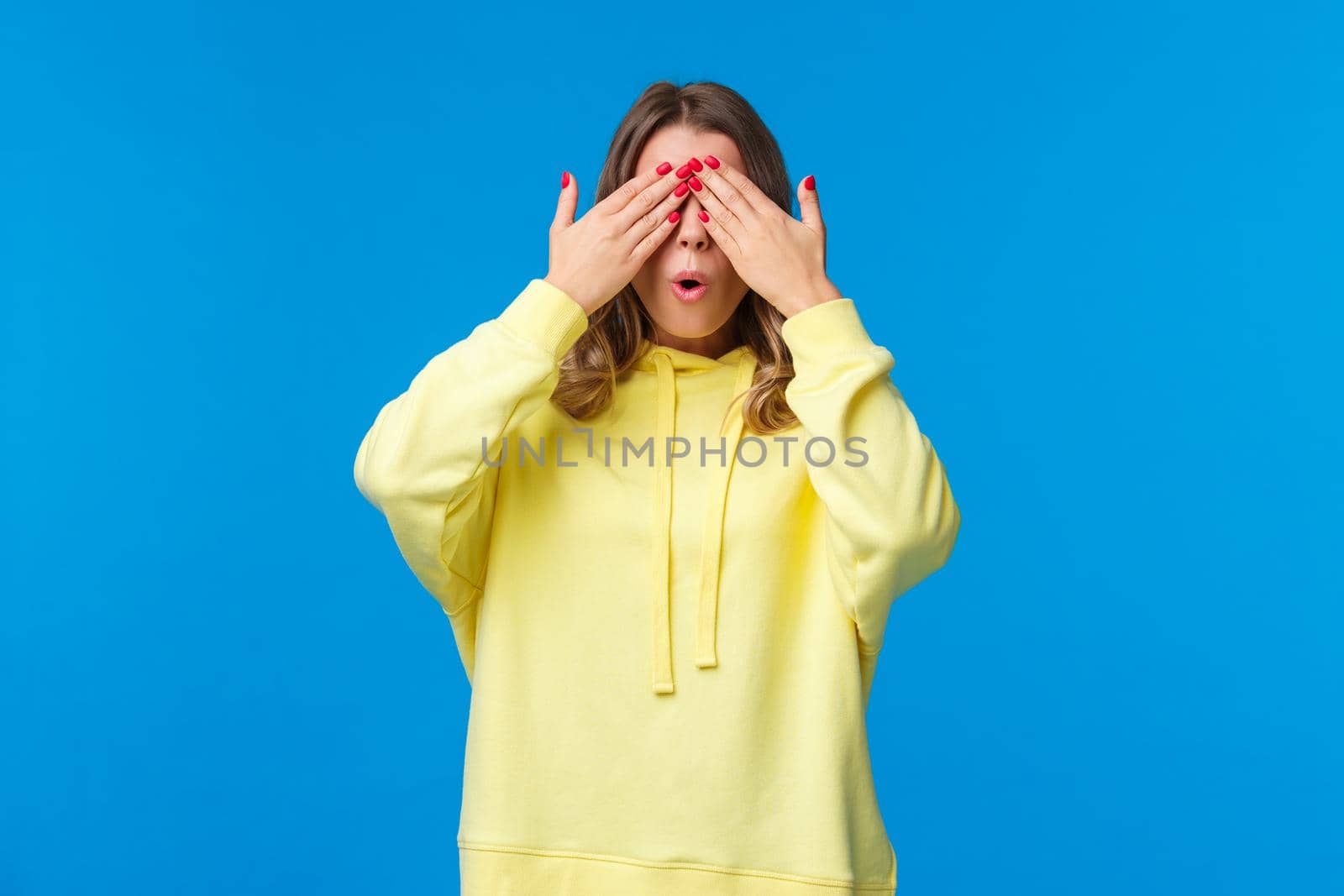 Girl fool around in playful mood, close eyes with hands count to ten, playing hide n seek or peekaboo, waiting for surprise gift, express curiosity and interest, stand blue background awaiting.