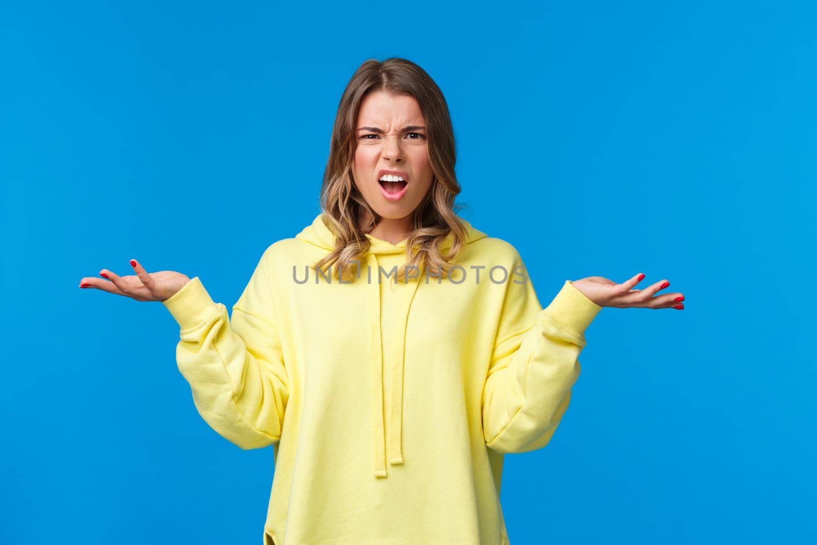 What problem wtf. Pissed-off frustrated and angry young blond caucasian girl shrugging with confused annoyed expression, cant understand what happened, dont know anything, blue background.