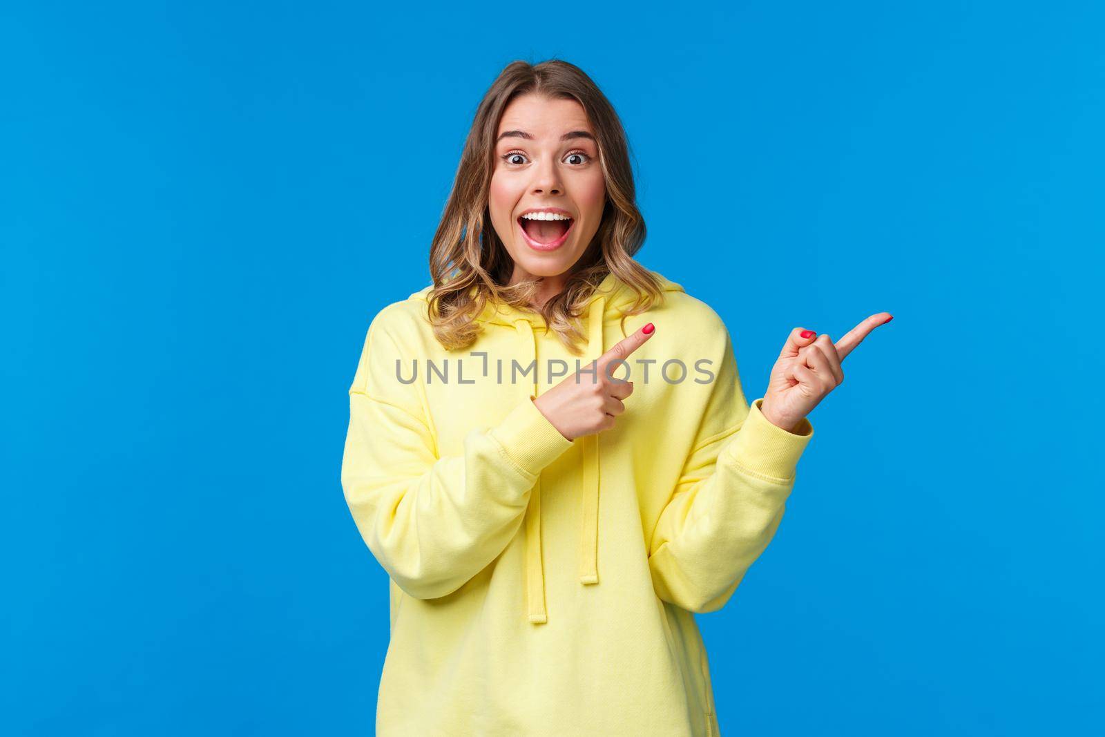 Wonderful news, come on hurry up and see. Impressed and excited cute happy blond girl pointing finger right and smiling surprised with astonished and excited face telling about awesome event by Benzoix