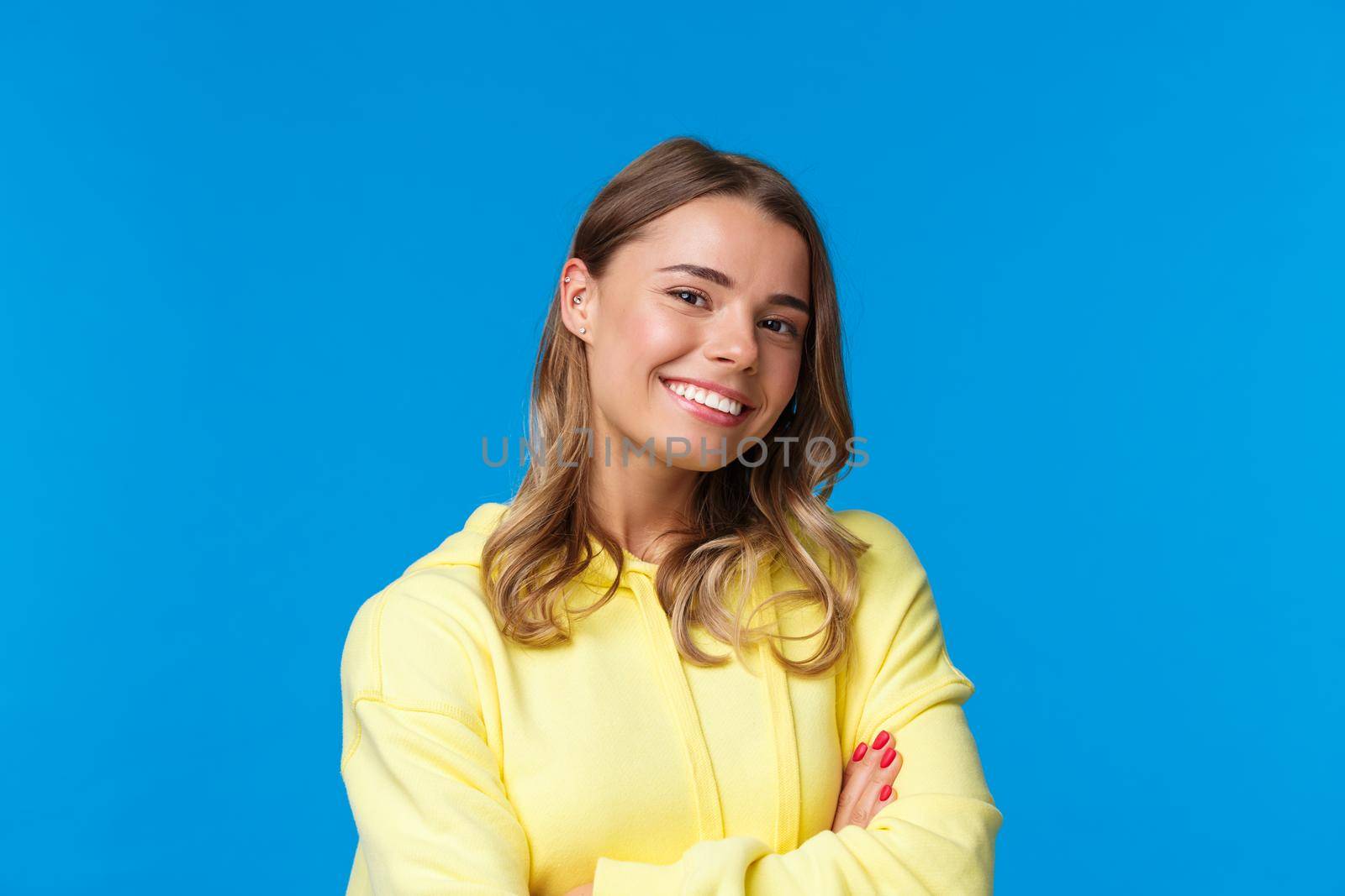 Close-up portrait of confident good-looking young blond girl with pierced ear, cross hands chest in professional self-assured pose, smiling enthusiastic, ready for job, blue background.