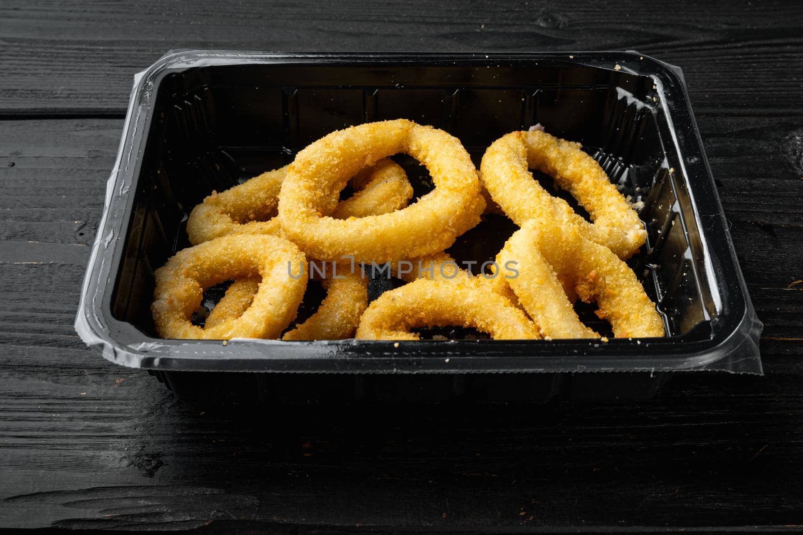 Raw crispy squid rings in breadcrumbs package set, on black wooden table background