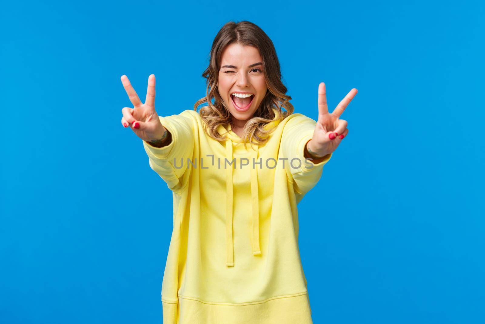 Stay positive. Kawaii joyful, friendly-looking smiling blond woman in yellow hoodie, stretch hands forward with peace gestures, show tongue and grinning, feel excited and upbeat.