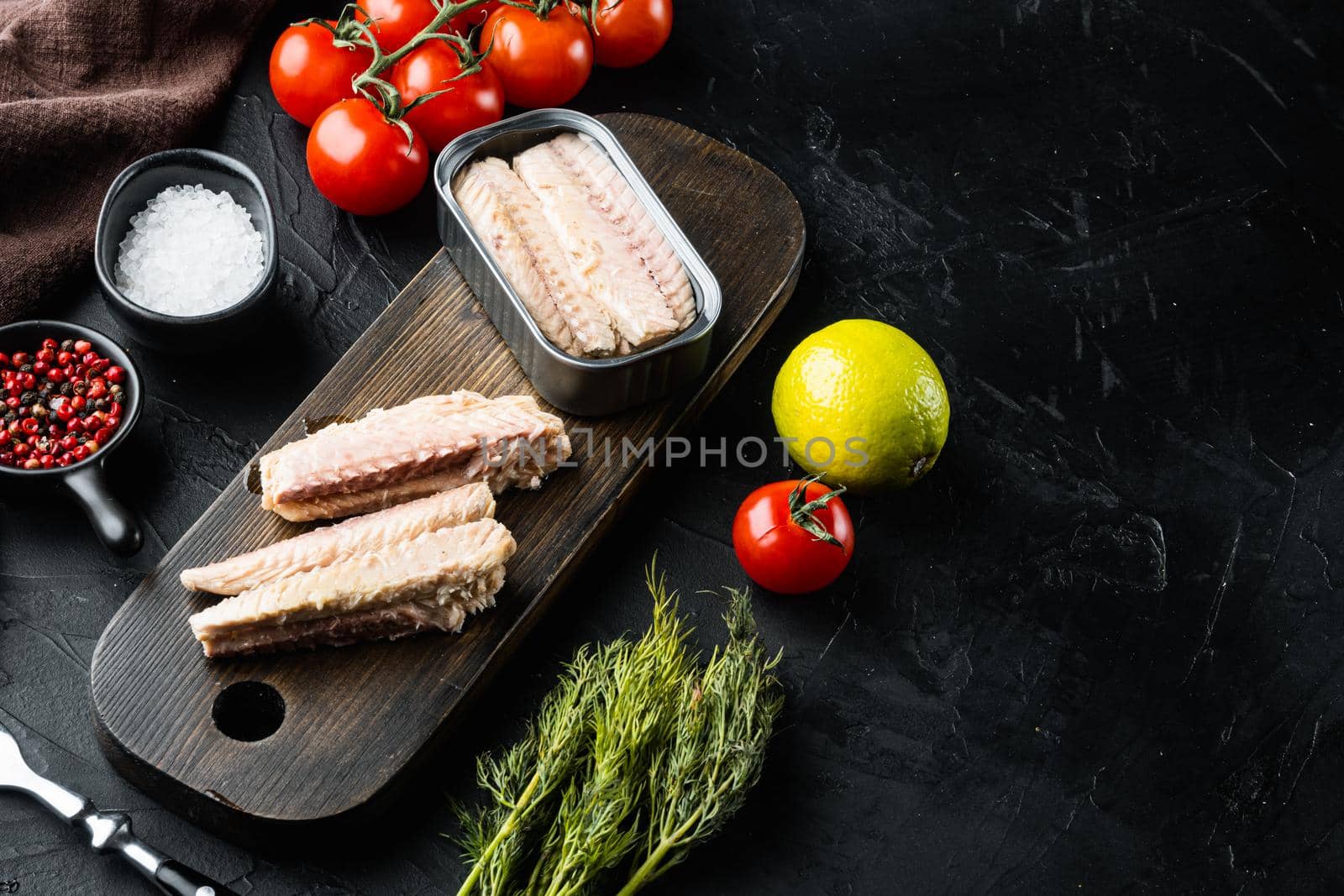 Canned Mackerel Fillets in Tin set, on wooden cutting board, on black background with herbs and ingredients, with copyspace and space for text