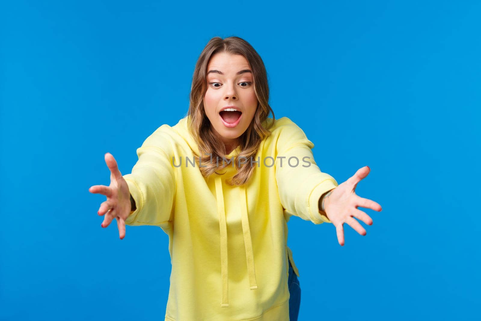 Girl trying to catch somthing, look focused and amused playing with kids, stretching hands and lean forward to read object with concentrated expression, standing blue background by Benzoix