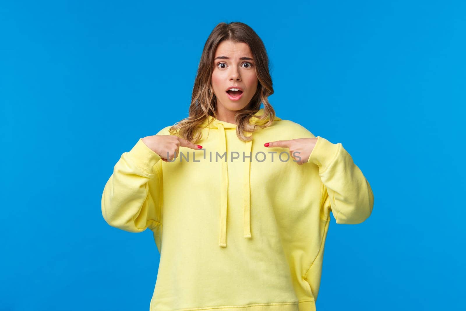 Surprised worried cute blond girl pointing at herself surprised with disbelief, cant understand if you really meant it, look camera nervously, being picked or chosen, stand blue background.
