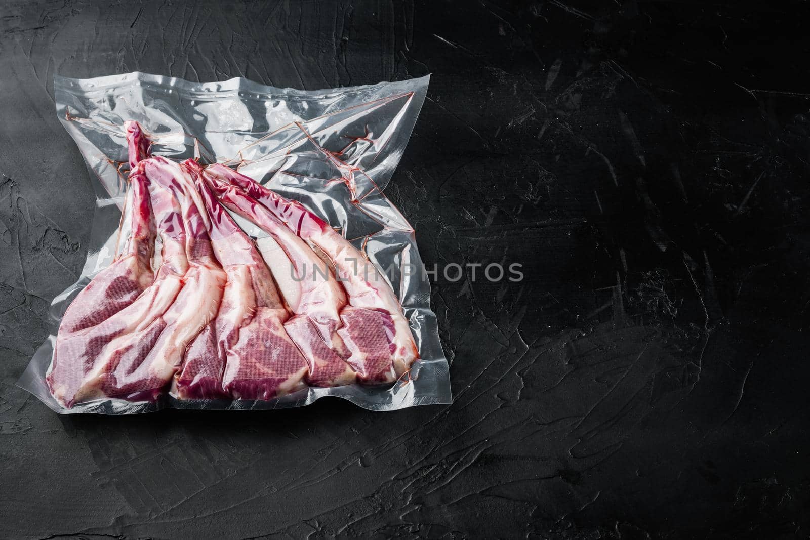 Lamb chops vacuumed for preservation or sous vide cooking set, on black stone background , with copyspace and space for text