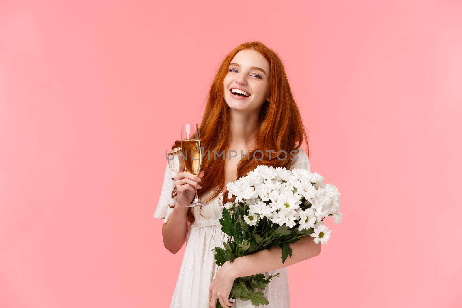 Attractive, cheerful b-day girl with red curly hair, laughing and looking camera carefree as speaking to friends during party, birthday celebration, holding bouquet white flowers and champagne glass by Benzoix