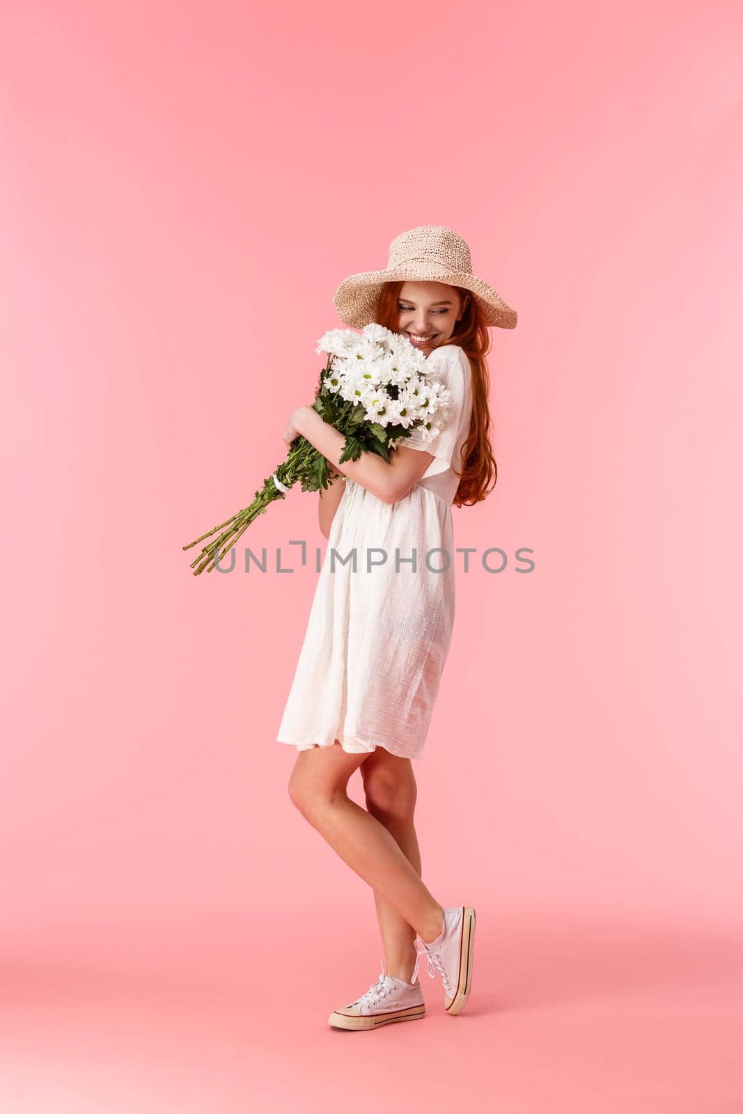 Full-length vertical shot lovely and romantic woman in straw hat, white dress, hugging and sniffing beautiful bouquet flowers, smiling and blushing, went on perfect valentines day date.