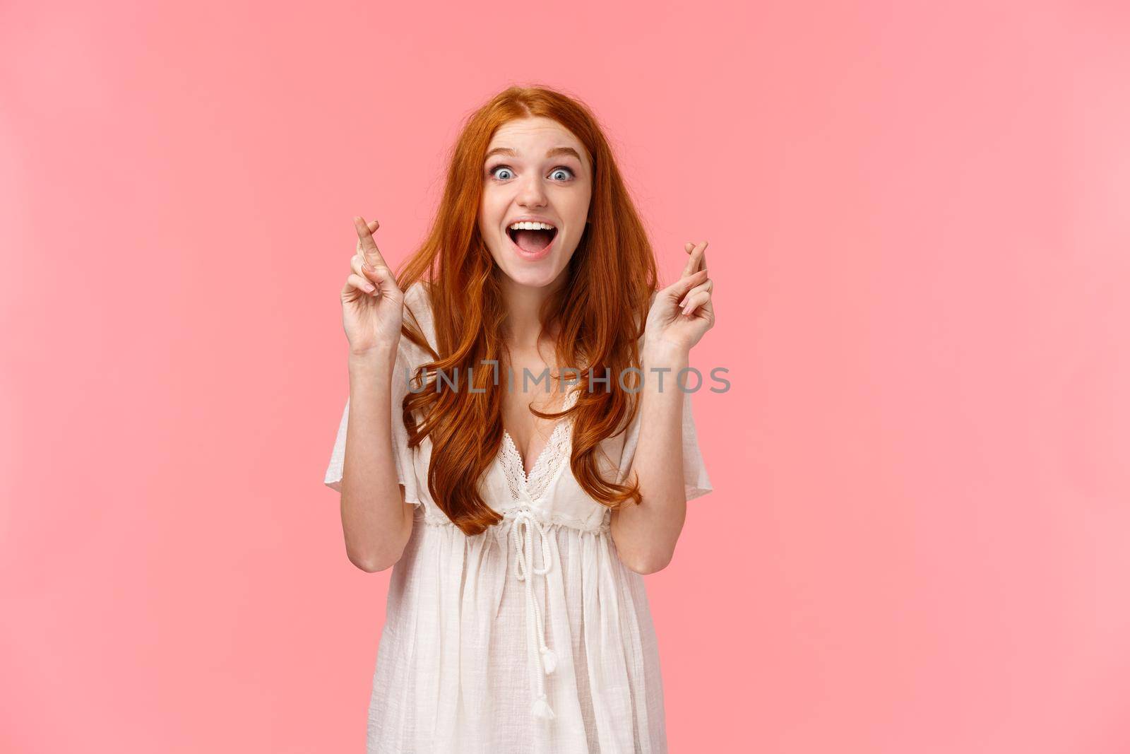 Lucky good-looking happy, excited redhead caucasian girl seeing her dream came true after praying with fingers crossed, looking amazed and surprised, rejoice from wish fulfilled, pink background.