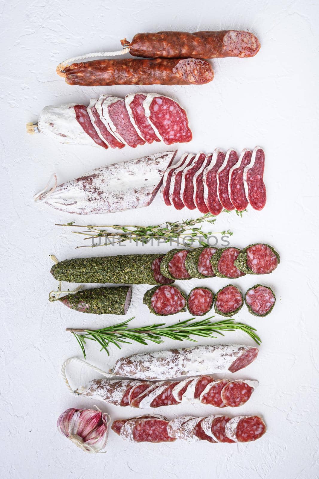 Variety of dry cured fuet and chorizosalami sausages, whole and sliced on white textured background, topview.