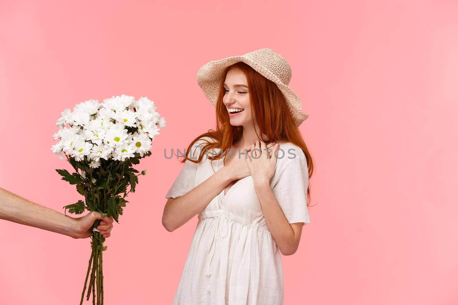 Gifts, celebration and tenderness concept. Surprised cute, alluring redhead woman in hat, dress, charmed with pleasant gift, holding hands on heart flattered, smiling, looking at bouquet flowers.