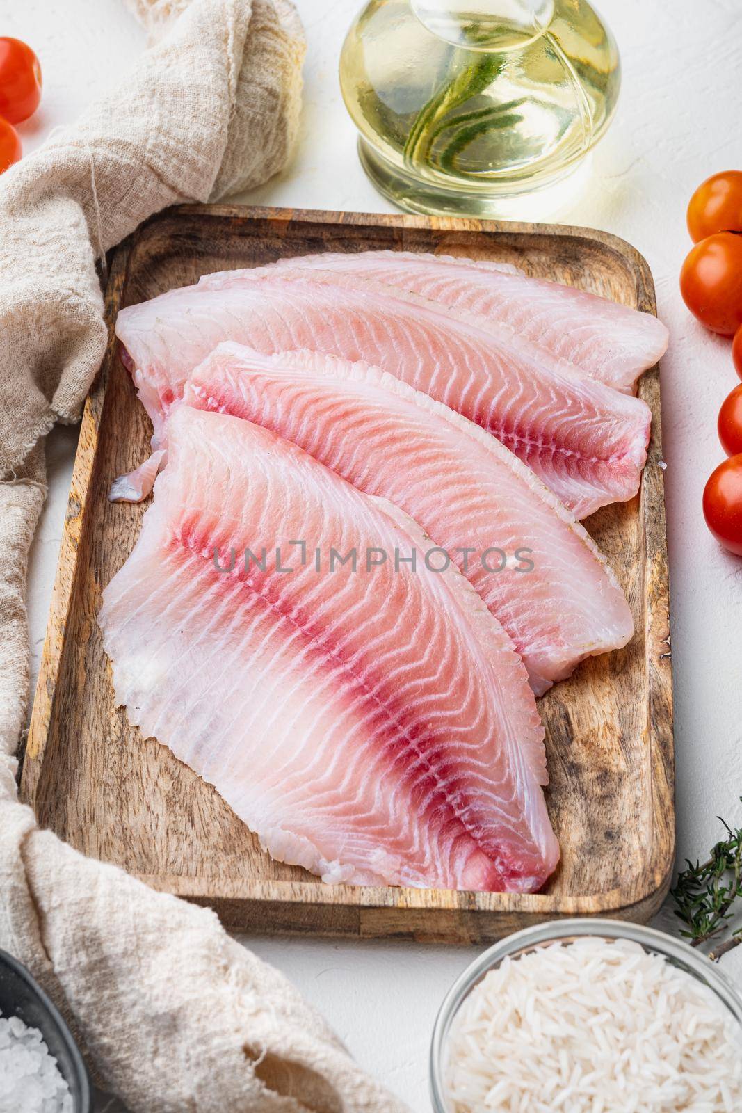 Raw white fish tilapia, with basmati rice and cherry tomatoes ingredients, on white background