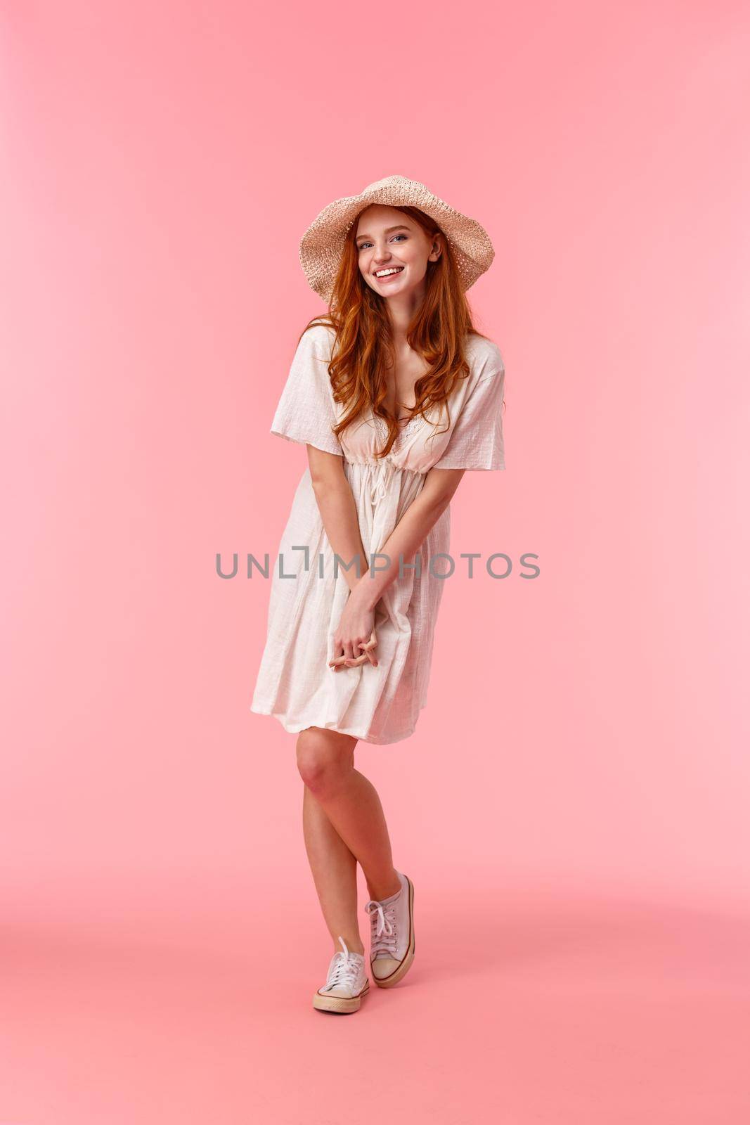Full-length vertical shot silly, coquettish caucasian redhead woman on romantic date, blushing looking flirty and giggle at camera, enjoying perfect company, great day, stand pink background.