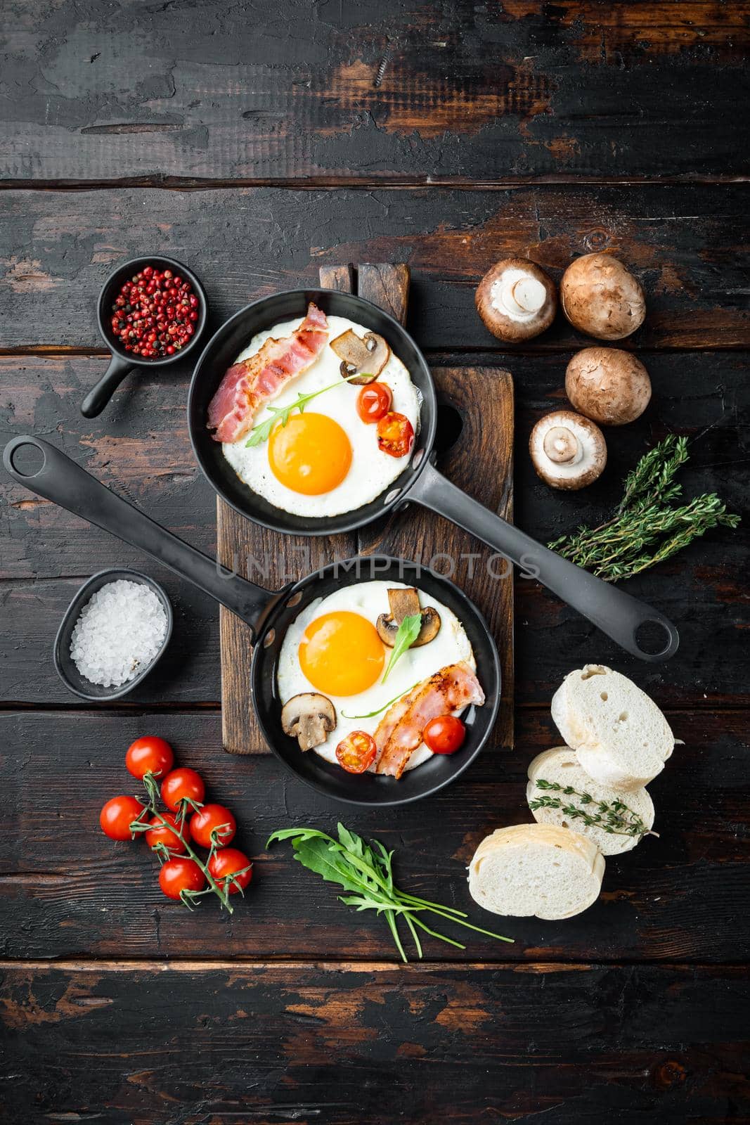 Fried eggs with bacon and vegetables in cast iron frying pan, on old dark wooden table background, top view flat lay by Ilianesolenyi