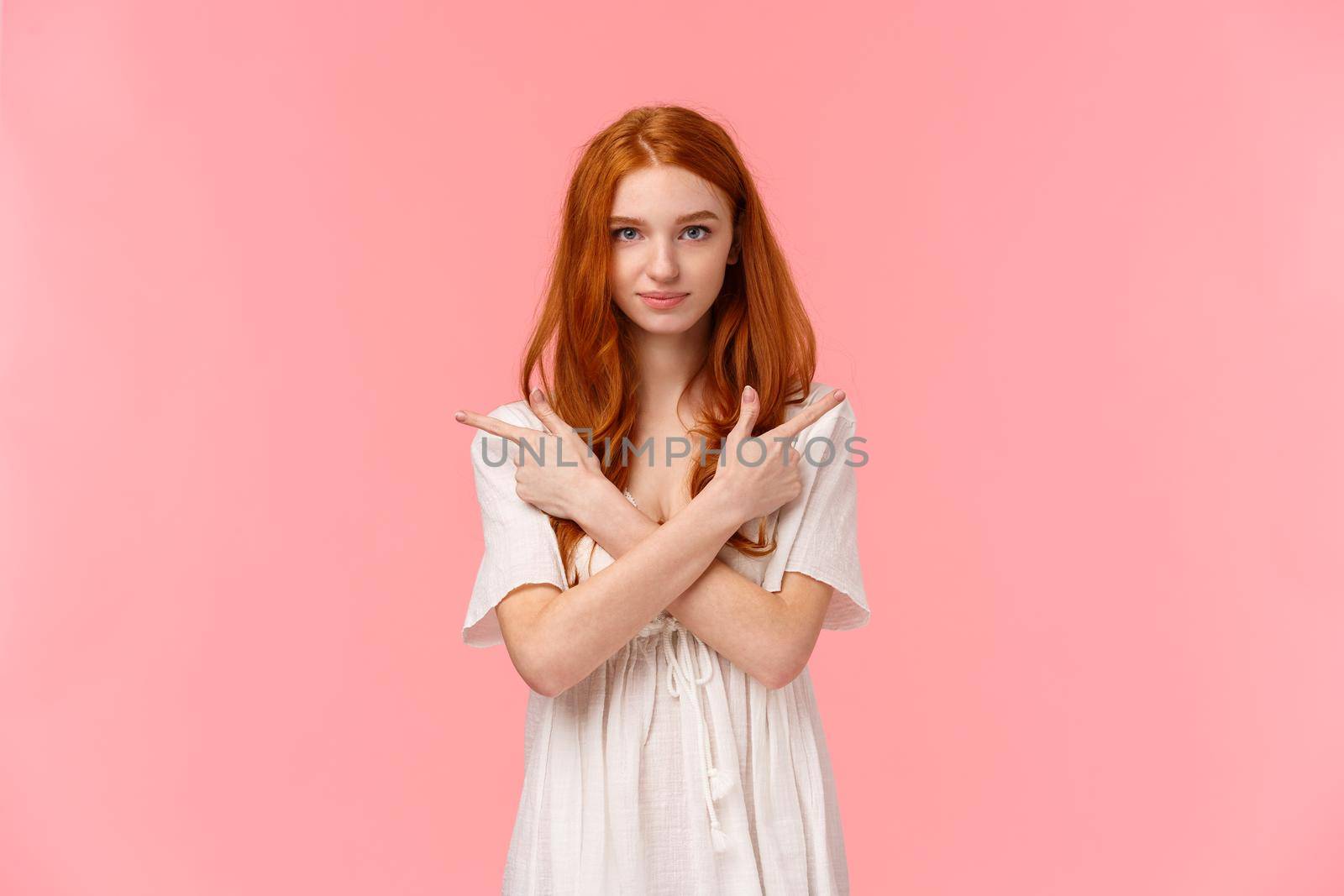 Girl asking you help her with making choice. Attractive redhead woman in white dress, cross hands over chest pointing sideways, showing left and right products and smiling camera, picking.