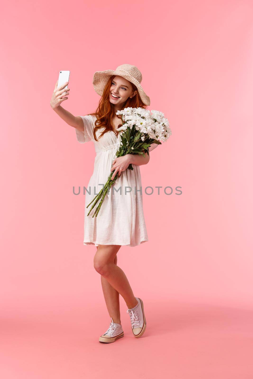 Full-length vertical shot lovely, romantic and silly redhead woman enjoying beautiful spring day, holding bouquet flowers and taking selfie on smartphone, smiling delighted by Benzoix
