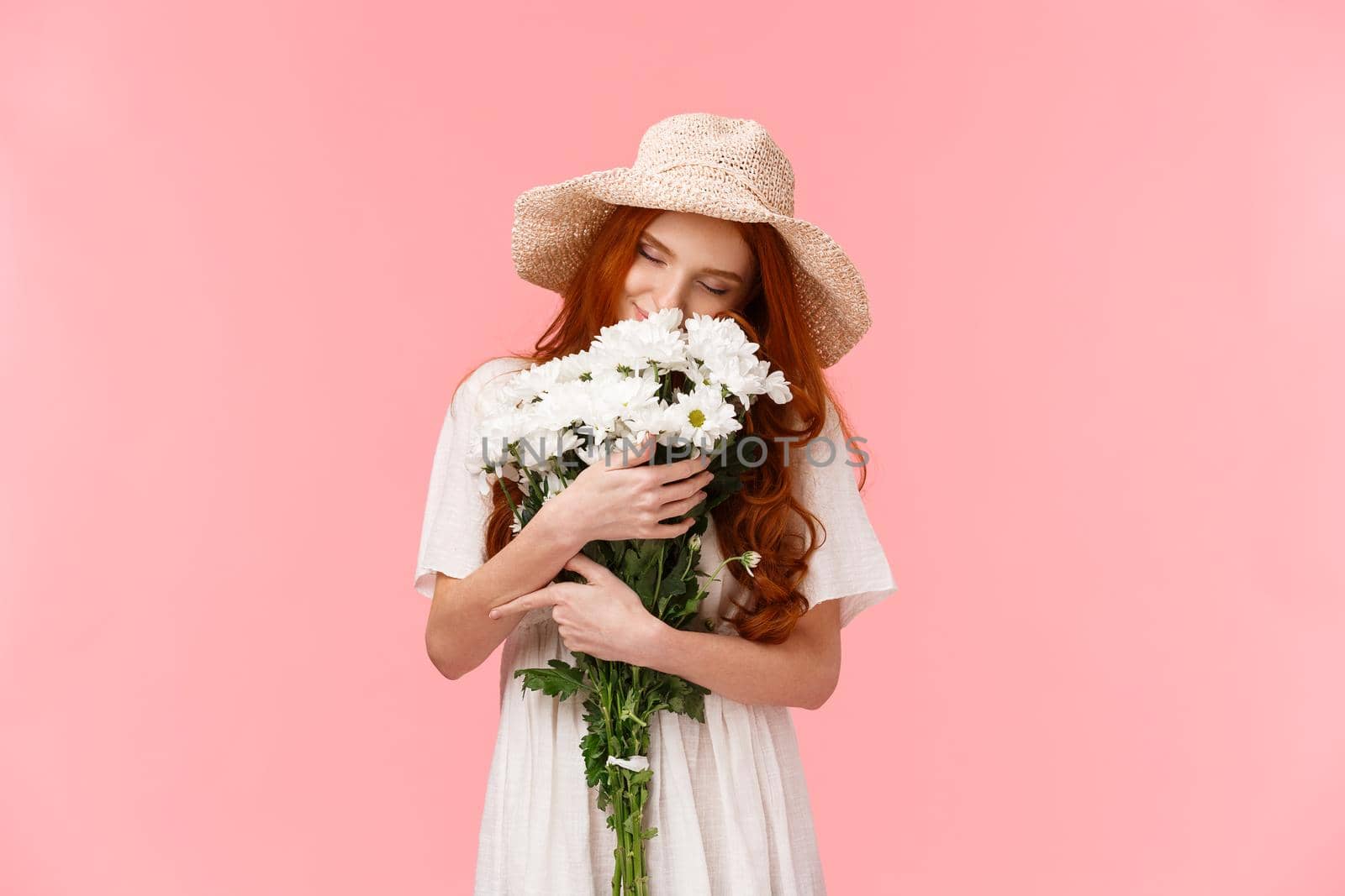 Romance, love and relationship concept. Romantic dreamy, alluring redhead girl sniffing flowers, close eyes and hugging beautiful bouquet, standing pink background. Copy space