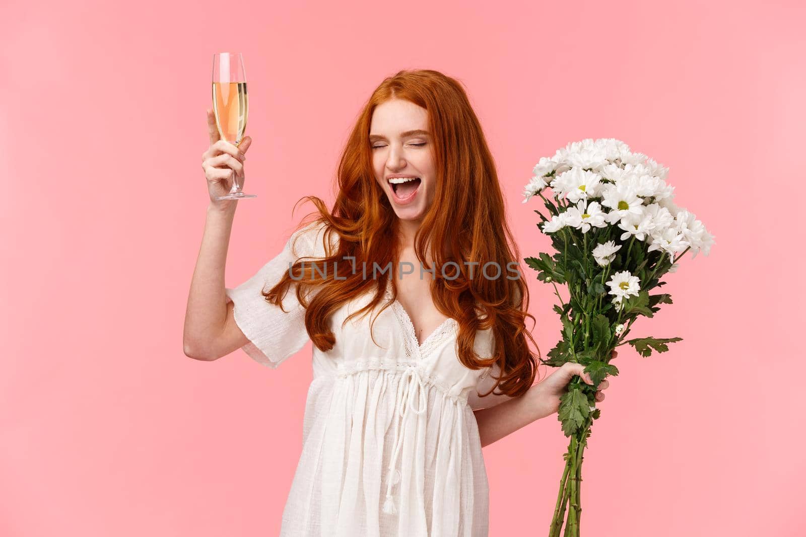 Excited and carefree good-looking redhead woman celebrating bachelorette party, scream yeah with closed eyes and relaxed expression, feeling awesome, holding bouquet flowers and raise champagne.