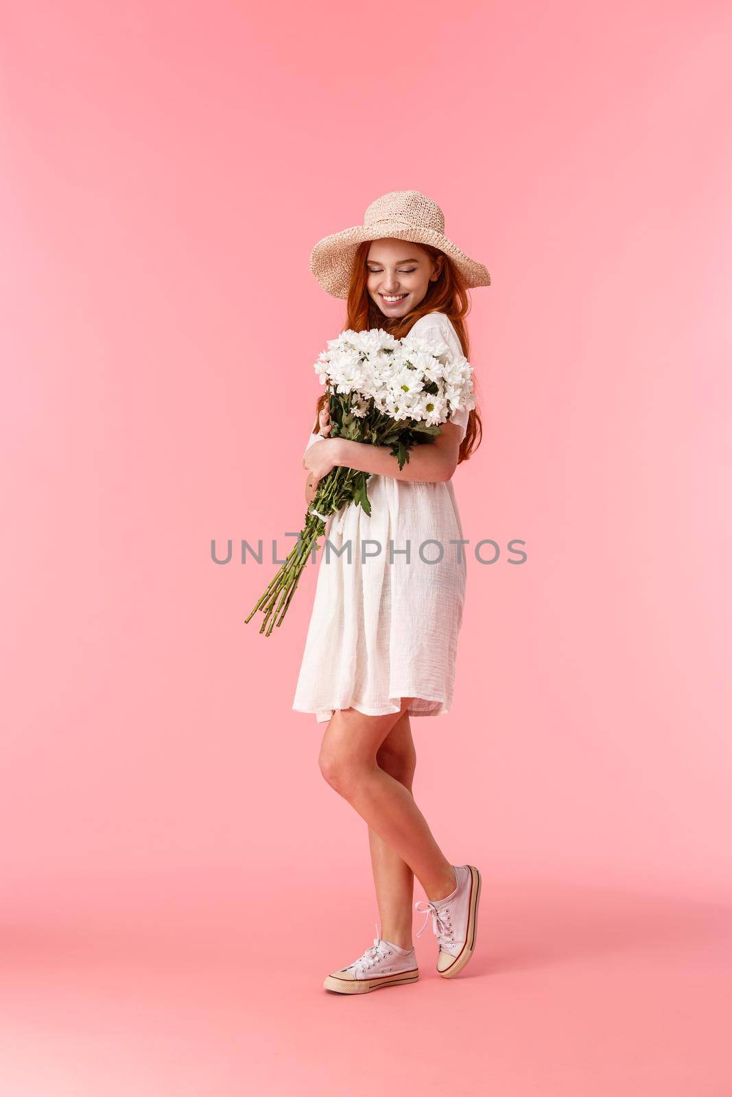 Full-length vertical shot lovely, sensual and romantic redhead woman in white dress, summer straw hat, receive beautiful bouquet on date, hugging flowers and grinning happy.