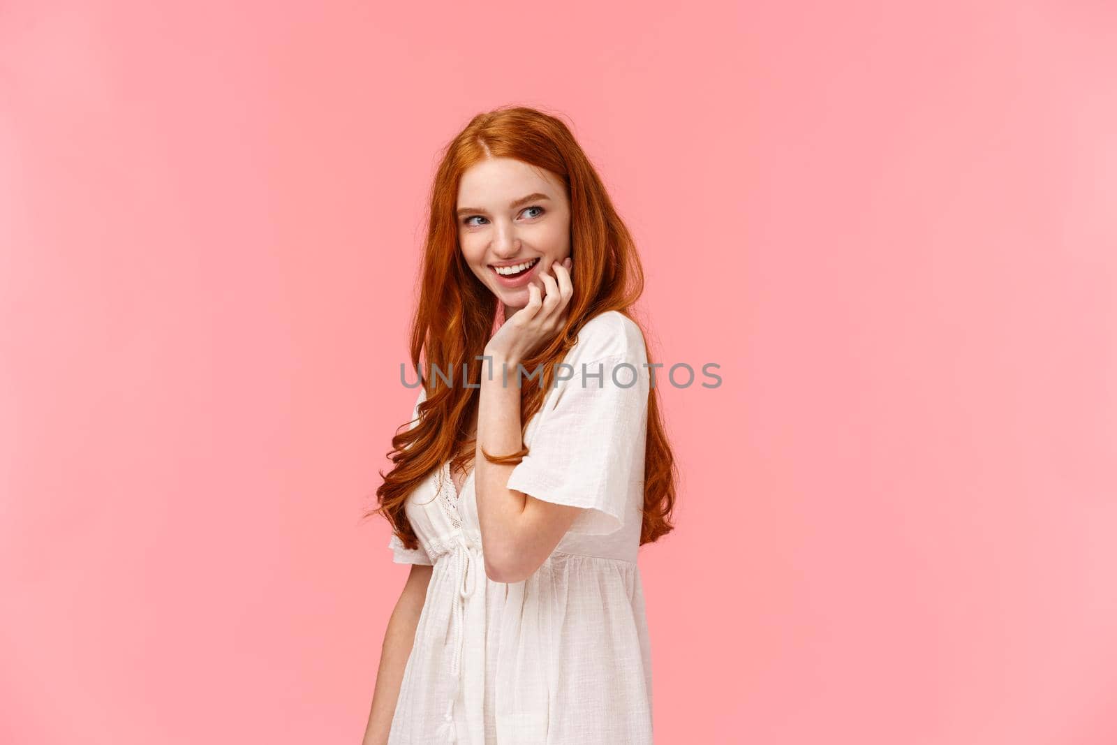 Waist-up portrait seducative and sensual, coquettish redhead flirty woman in white dress, glancing right smiling curiously, standing pink background intrigued, checking out something interesting.