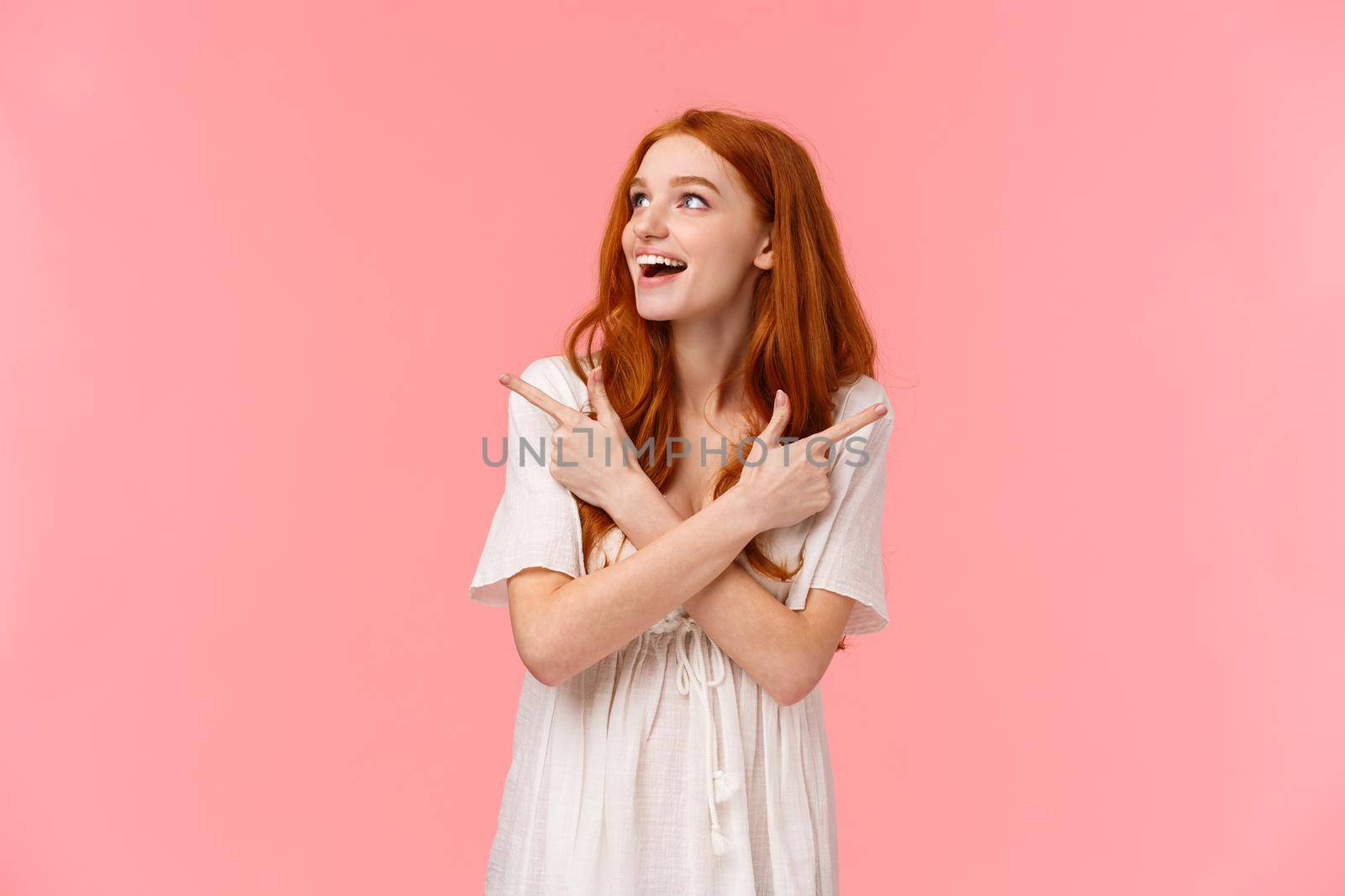 Dreamy attractive redhead female, looking around wondered and amused with happy smile, glance left as pointing sideways, left and right products, making final choice what buy, pink background.
