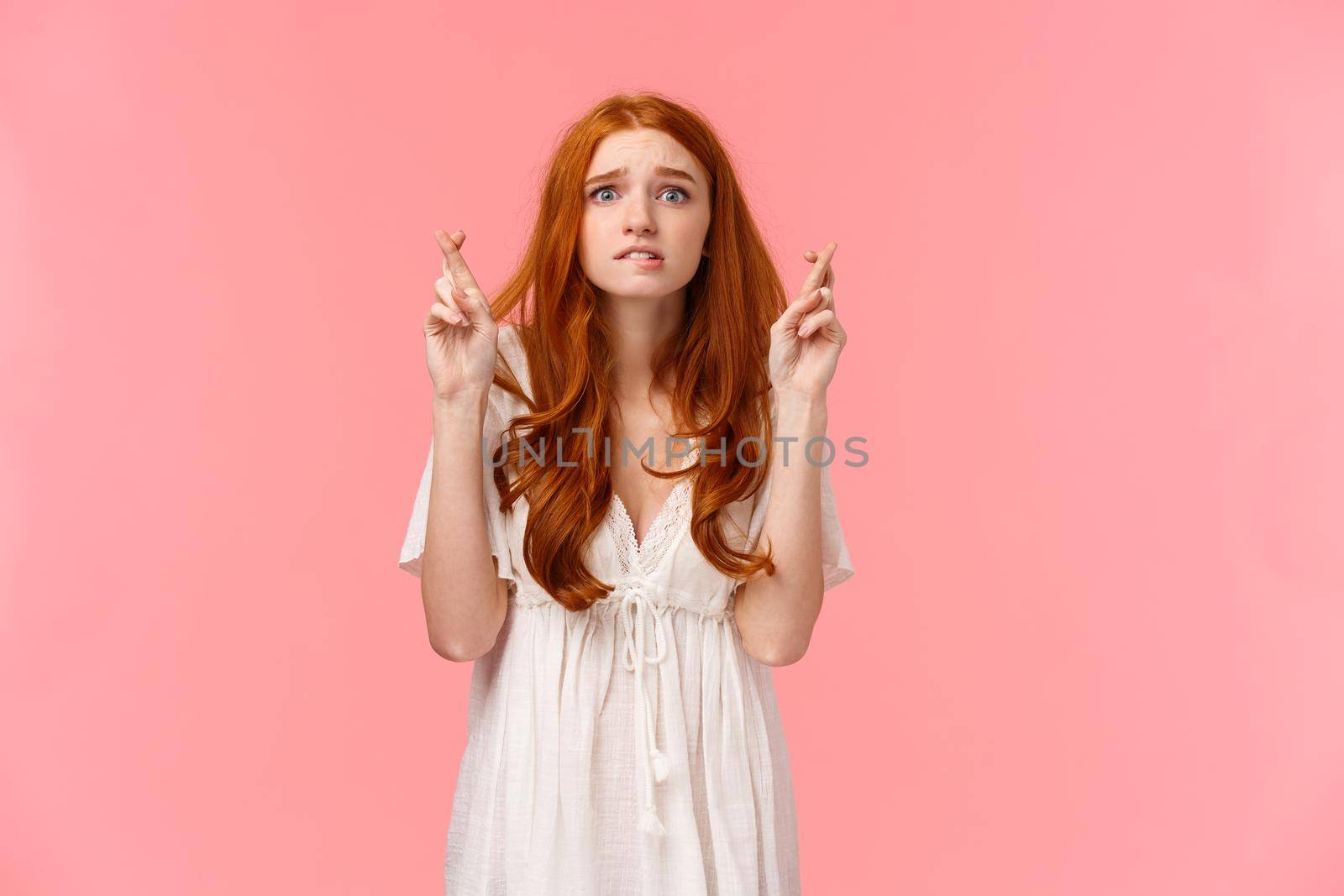 Nervous cute teenage redhead girl praying someting good happen, wish enter cool unversity, waiting enrollment info, cross fingers good luck, biting lip anxious, standing pink background.