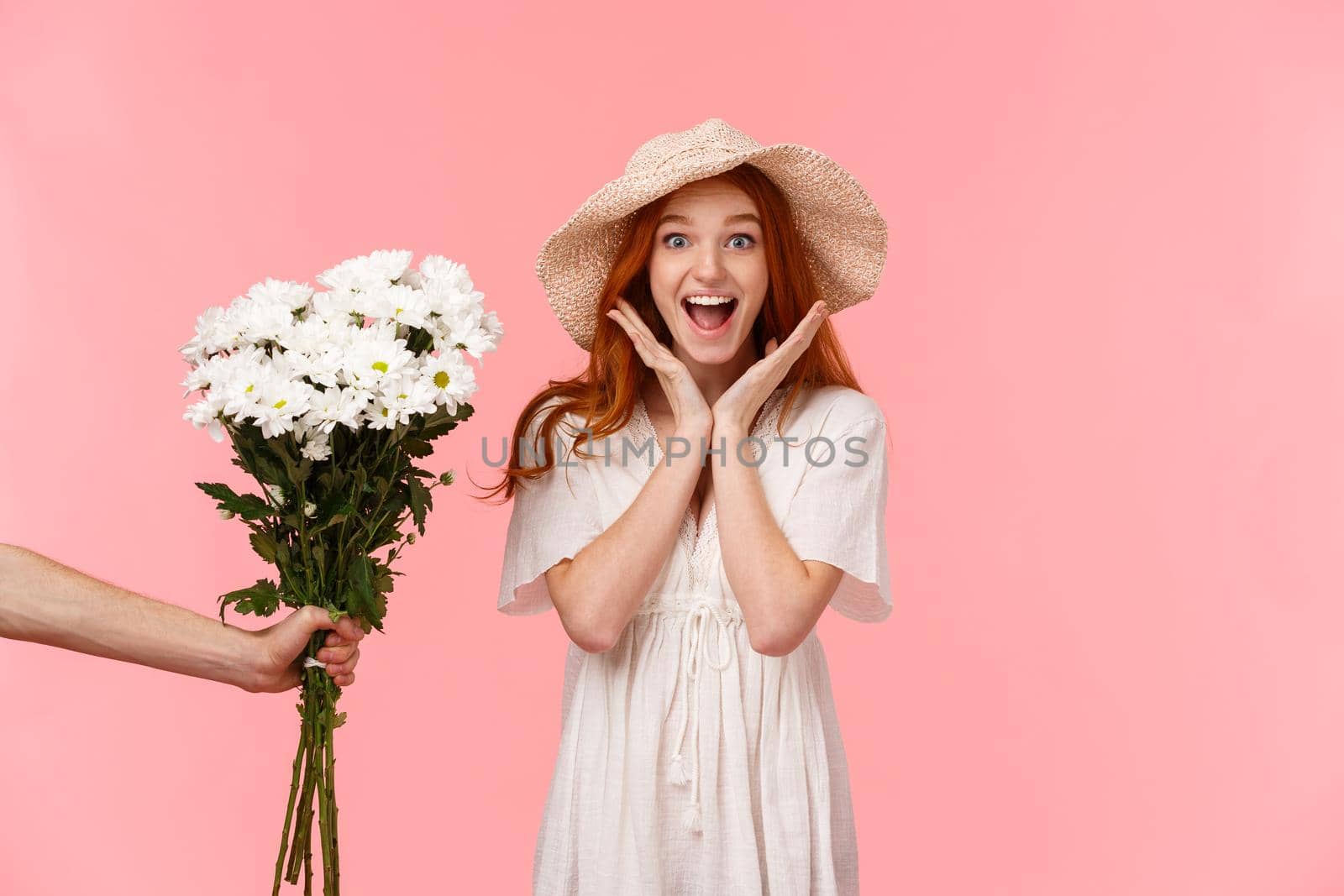 Surprises, celebration and holidays concept. Astonished happy and cheerful smiling redhead girl scream from happiness and joy, looking enthusiastic as someone giving her flowers, pink background.