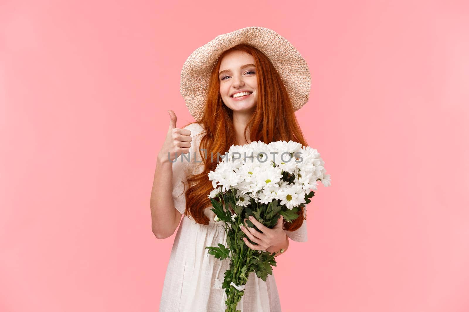Woman prepared present for mothers day, standing cheerful and delighted, bought white beautiful flowers, showing thumb-up and smiling satisfied as holding bouquet, stand pink background.