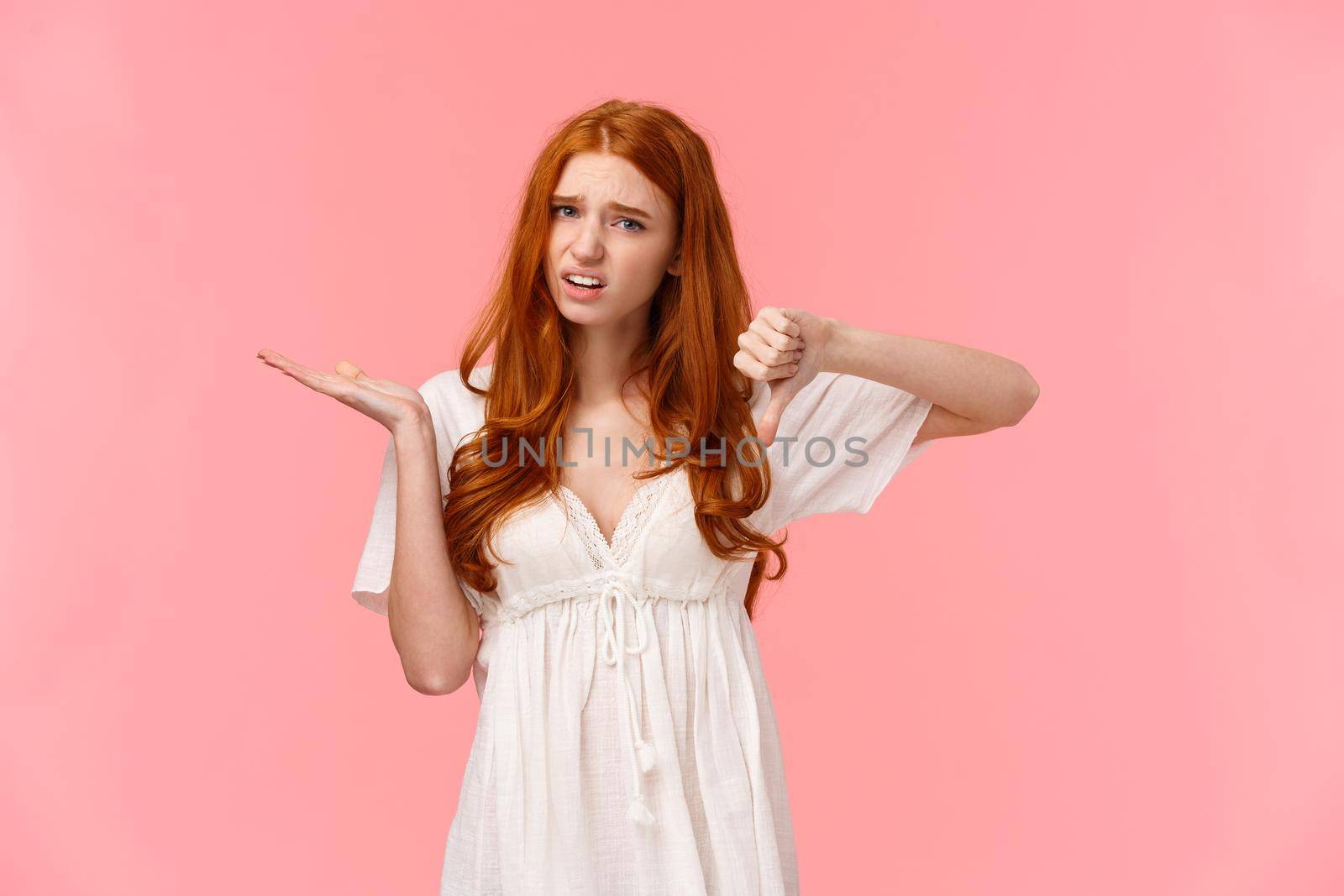 Skeptical displeased redhead female customer have her negative opinion, pointing at something bothering and really bad, grimacing unsatisfied, show thumb-down in dislike, disagree gesture.