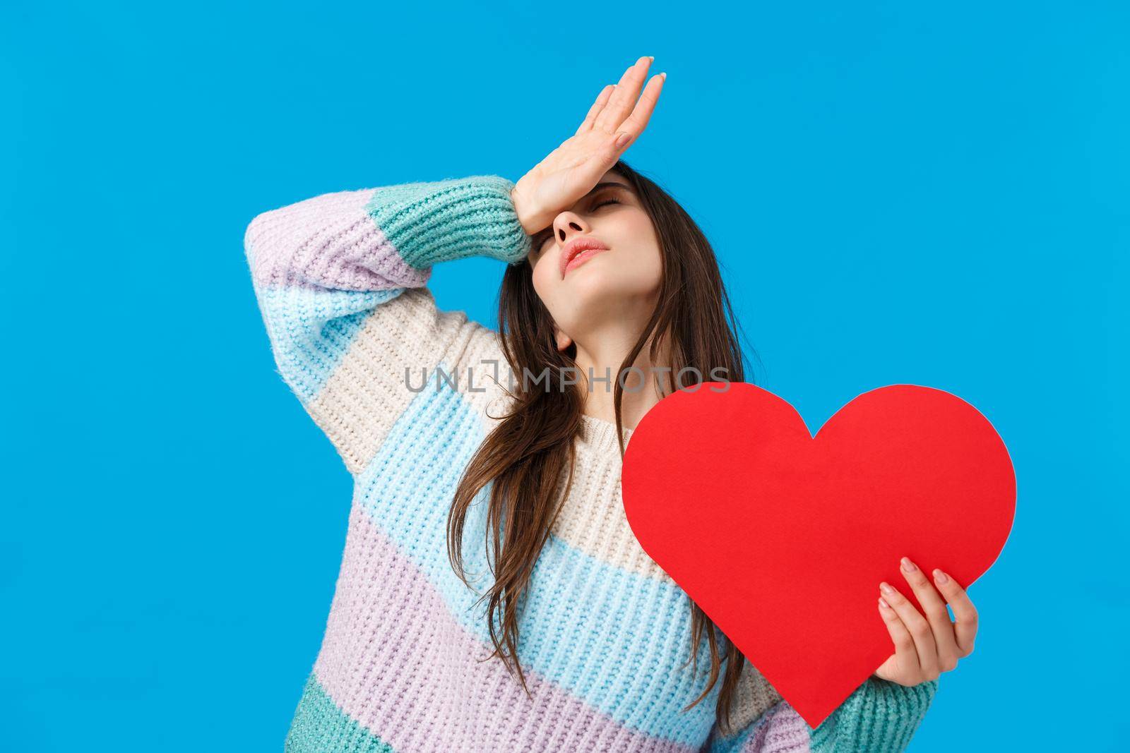 Passion, feelings and romance on valentines day concept. Passionate tender attractive woman in love, losing her mind over love, fain and hold hand on forehead, holding cute red heart sign.