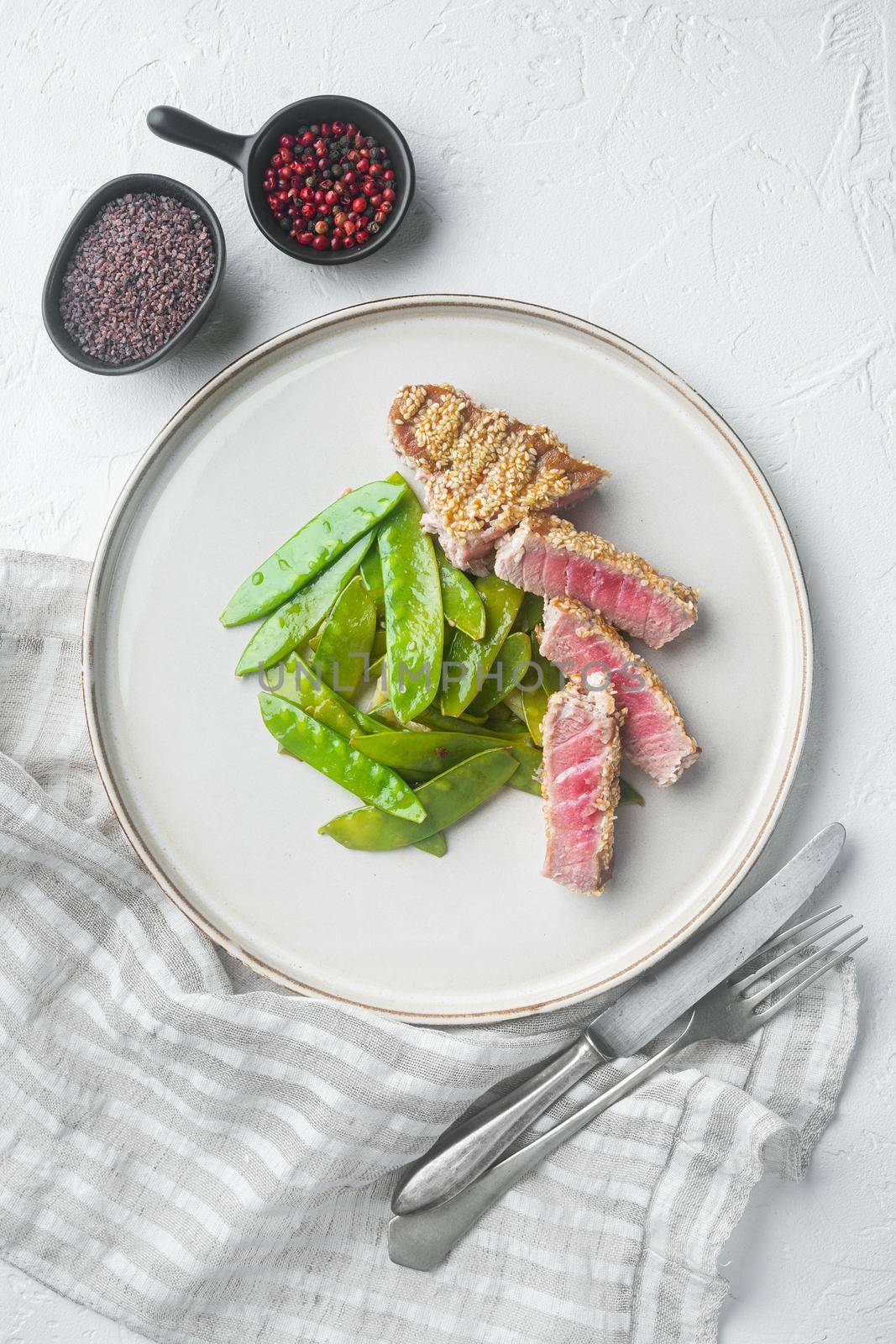 Grilled Ahi Tuna Steak set with spring onions and sugar snap peas, on plate, on white stone background, top view flat lay