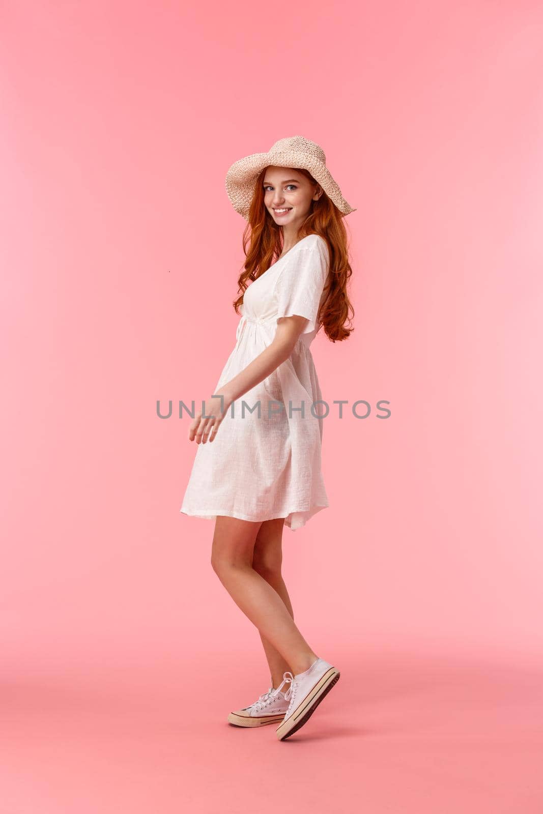 Full-length vertical shot elegant, feminine young redhead woman having walk, enjoying warm lovely spring days, turn back to smile at camera, wearing white dress and straw hat, pink background by Benzoix