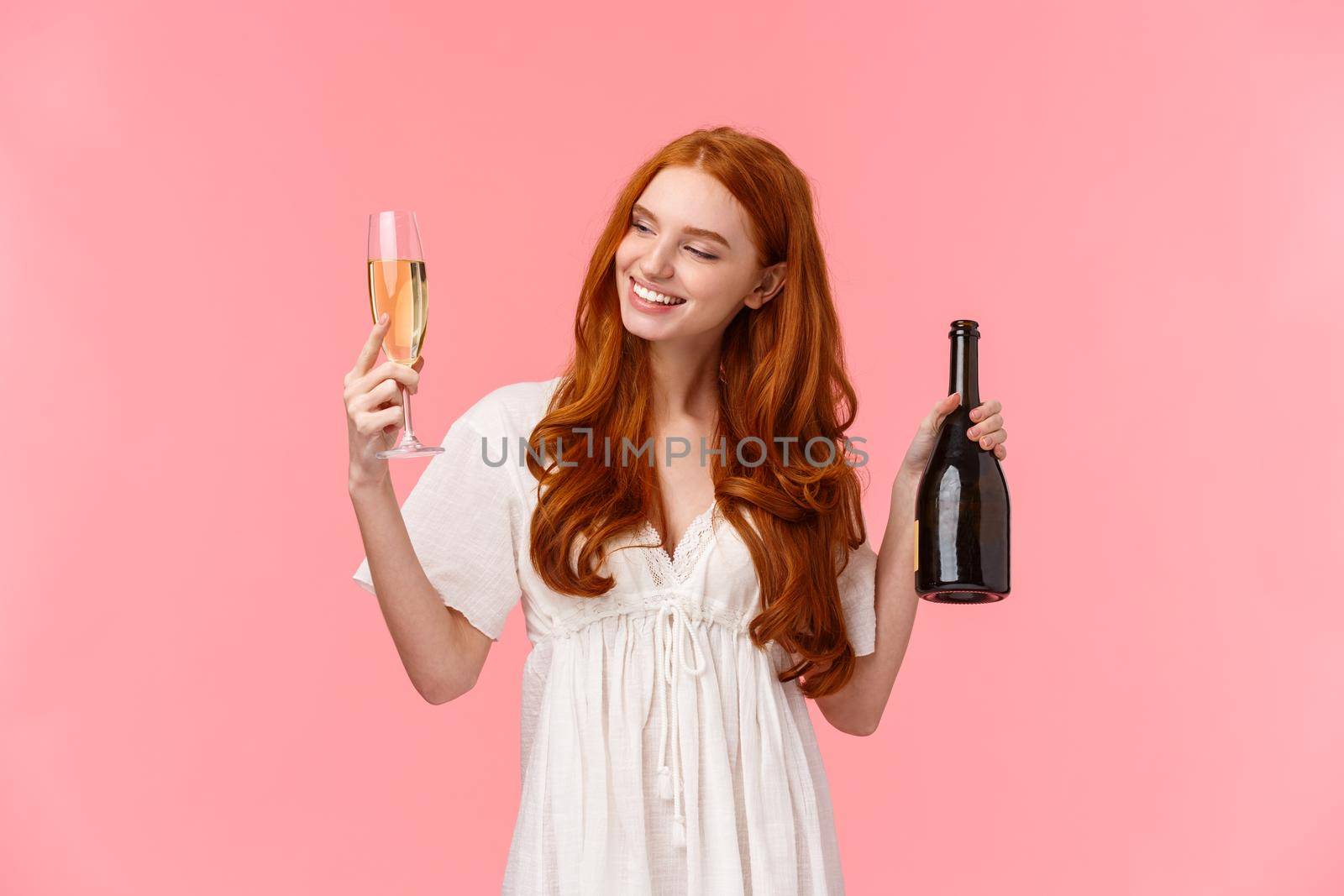 Girl feeling relaxed and happy slightly drunk smiling and looking at poured glass, holding and drinking champagne, grinning, partying on honey moon, standing pink background.