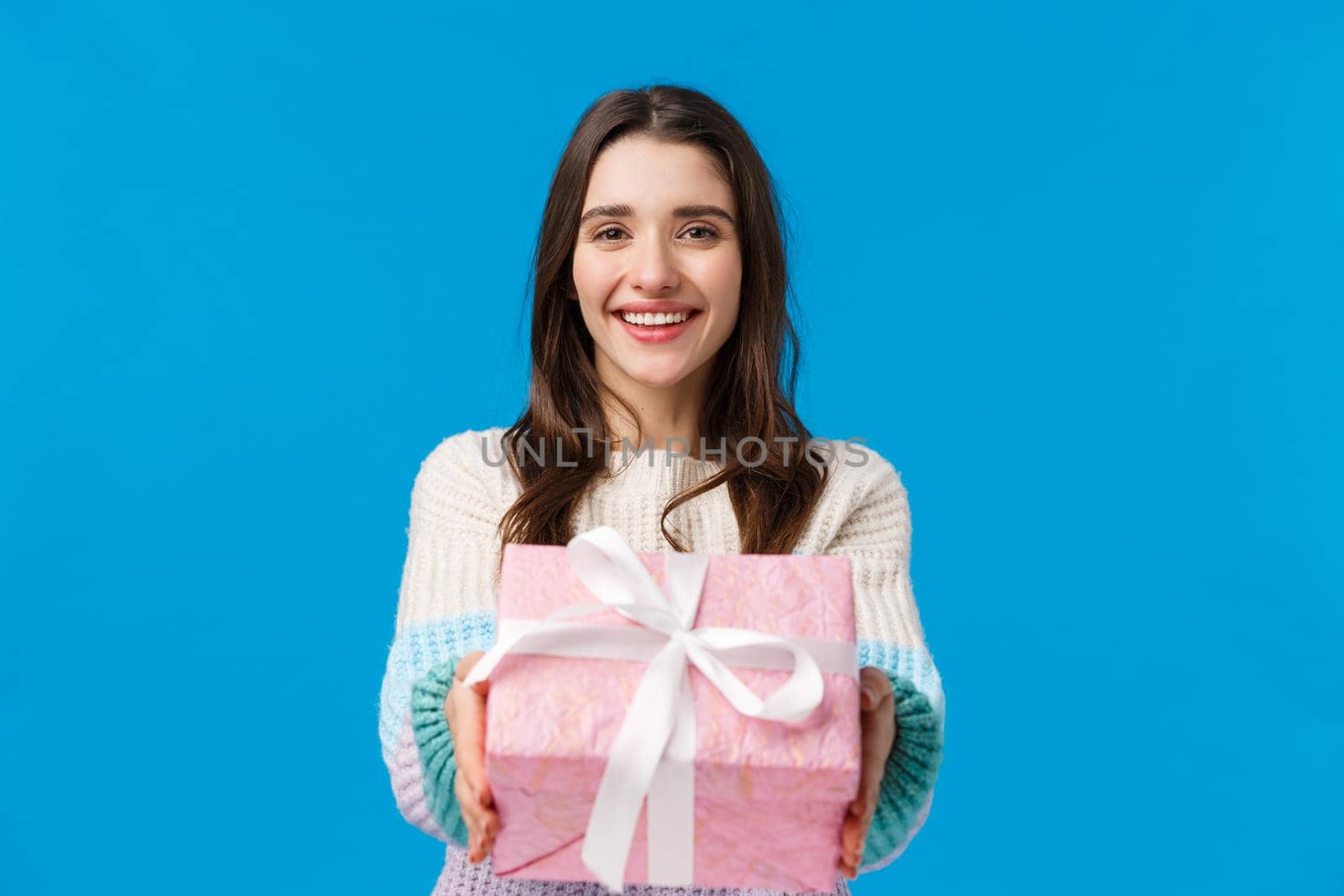 Here its for you. Cheerful, lovely and friendly smiling brunette woman extending hands and giving present, congratulating with birthday, happy holidays, made gift, standing blue background.