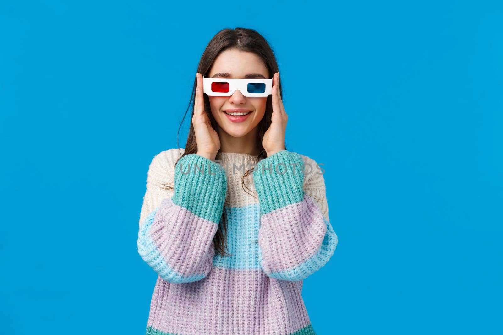 Turn on, lets start. Attractive amused and happy smiling young woman in winter sweater, wear 3d glasses and grinning, tempt see new premiere in cinema, watching movie over blue background by Benzoix
