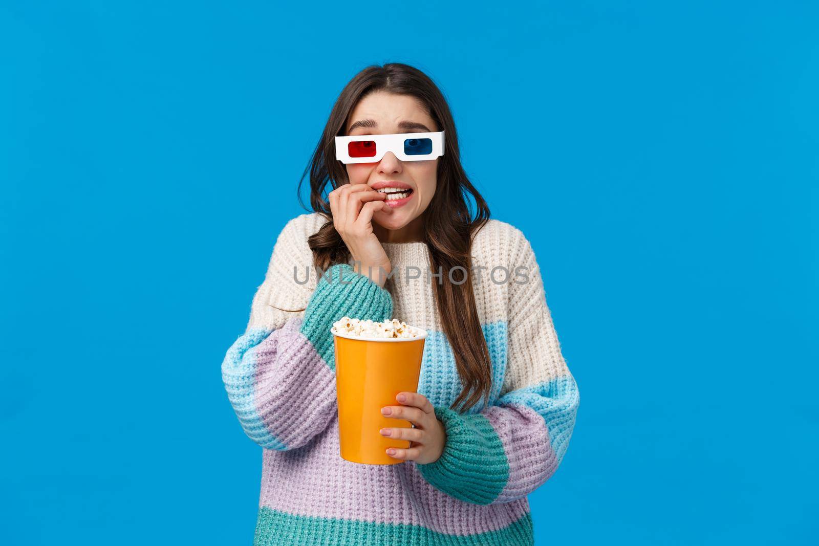 Waist-up portrait astonished and scared young brunette girl in winter sweater, watchign scary movie, premiere in cinema, wear 3d glasses, biting fingernails and holding popcorn, afraid of film scene.