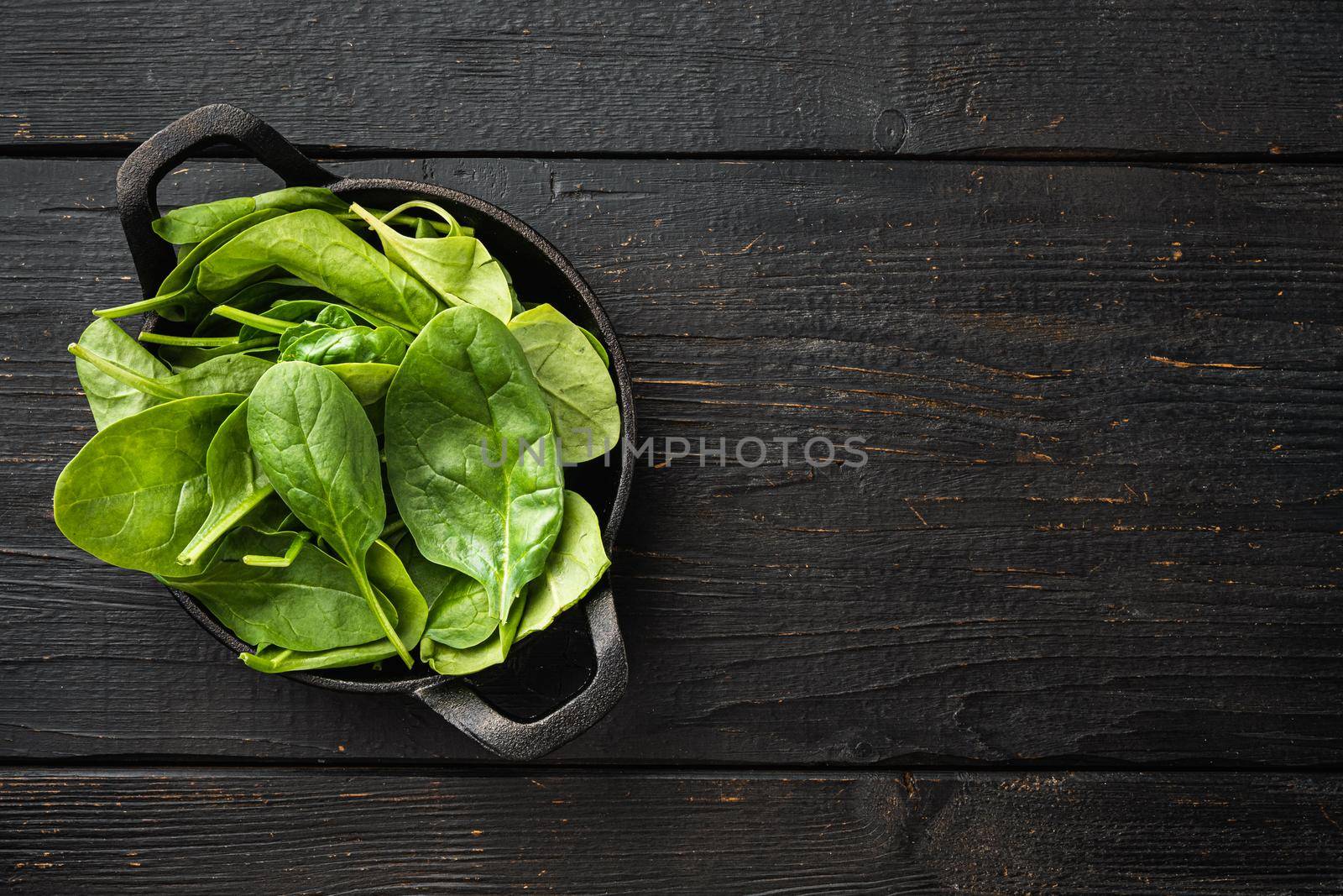 Bundle of fresh spinach set, in frying cast iron pan or pot, on black wooden table background, top view flat lay, with copy space for text