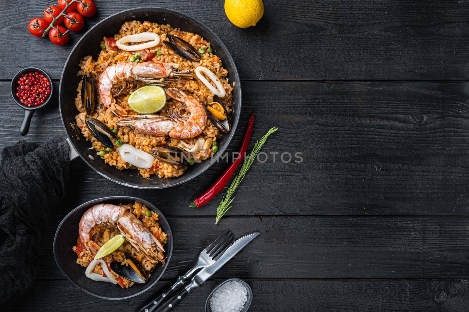 Valenciana seafood paella in bowl and frying pan on black wooden planks, top view with space for text, food photo.